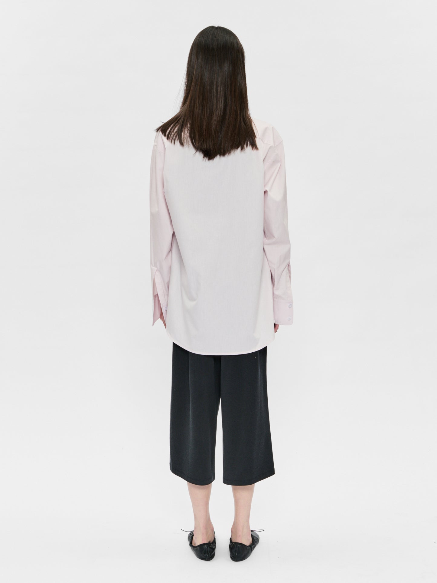 Person wearing a light pink blouse and black pants on a white background