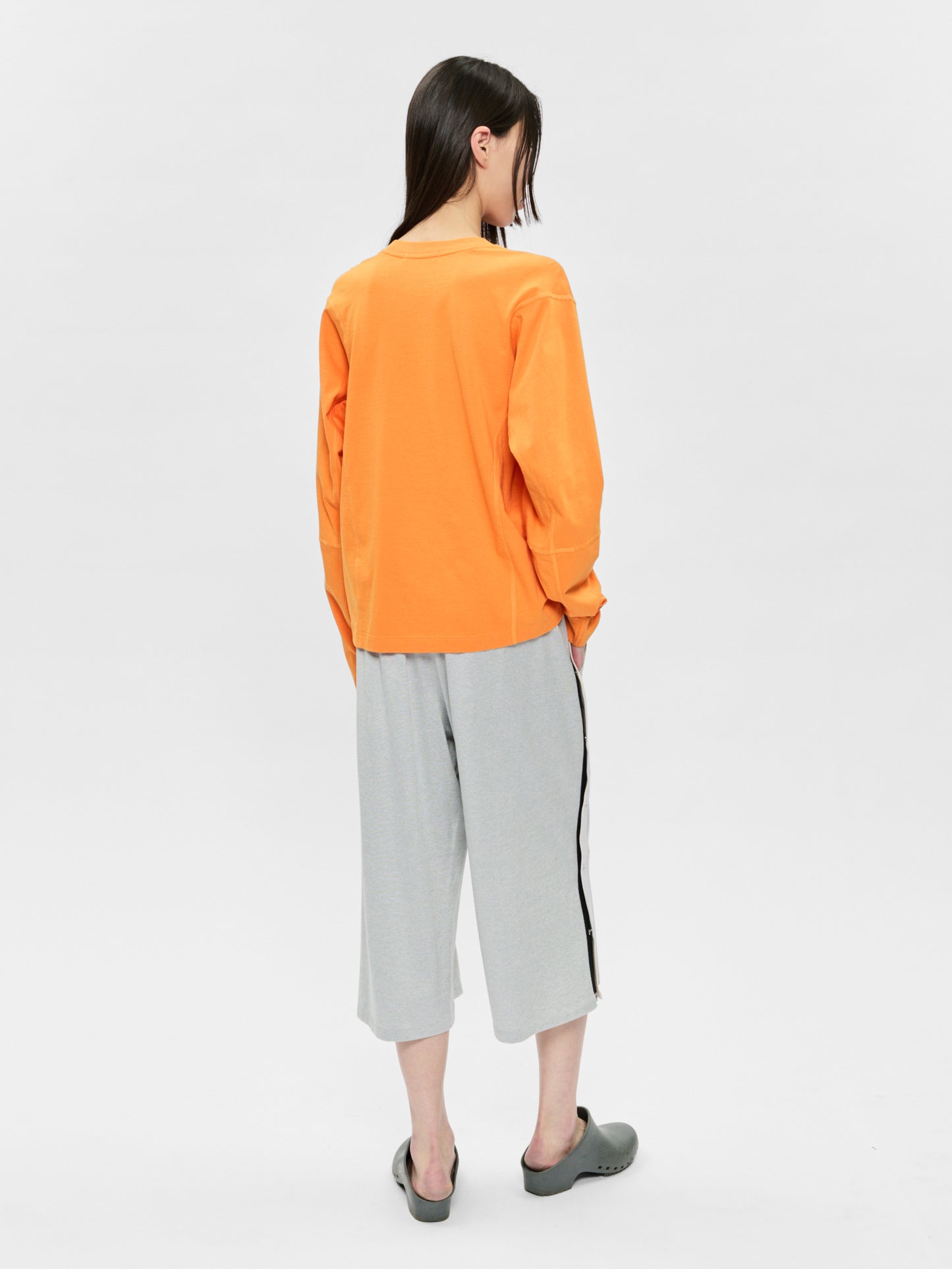 Person wearing an orange sweatshirt and gray pants on a white background