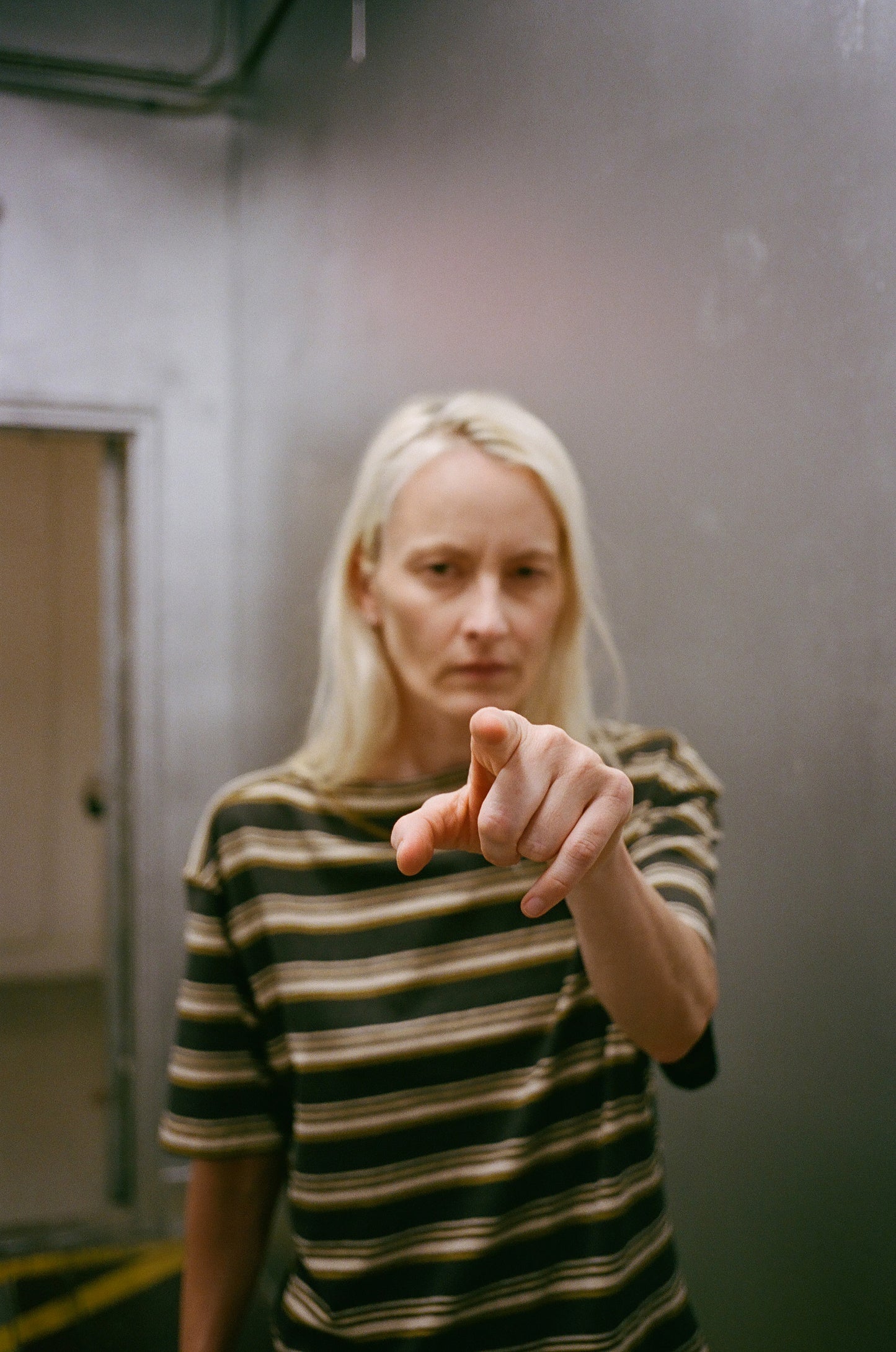 Person wearing a striped shirt pointing towards the camera in an indoor setting