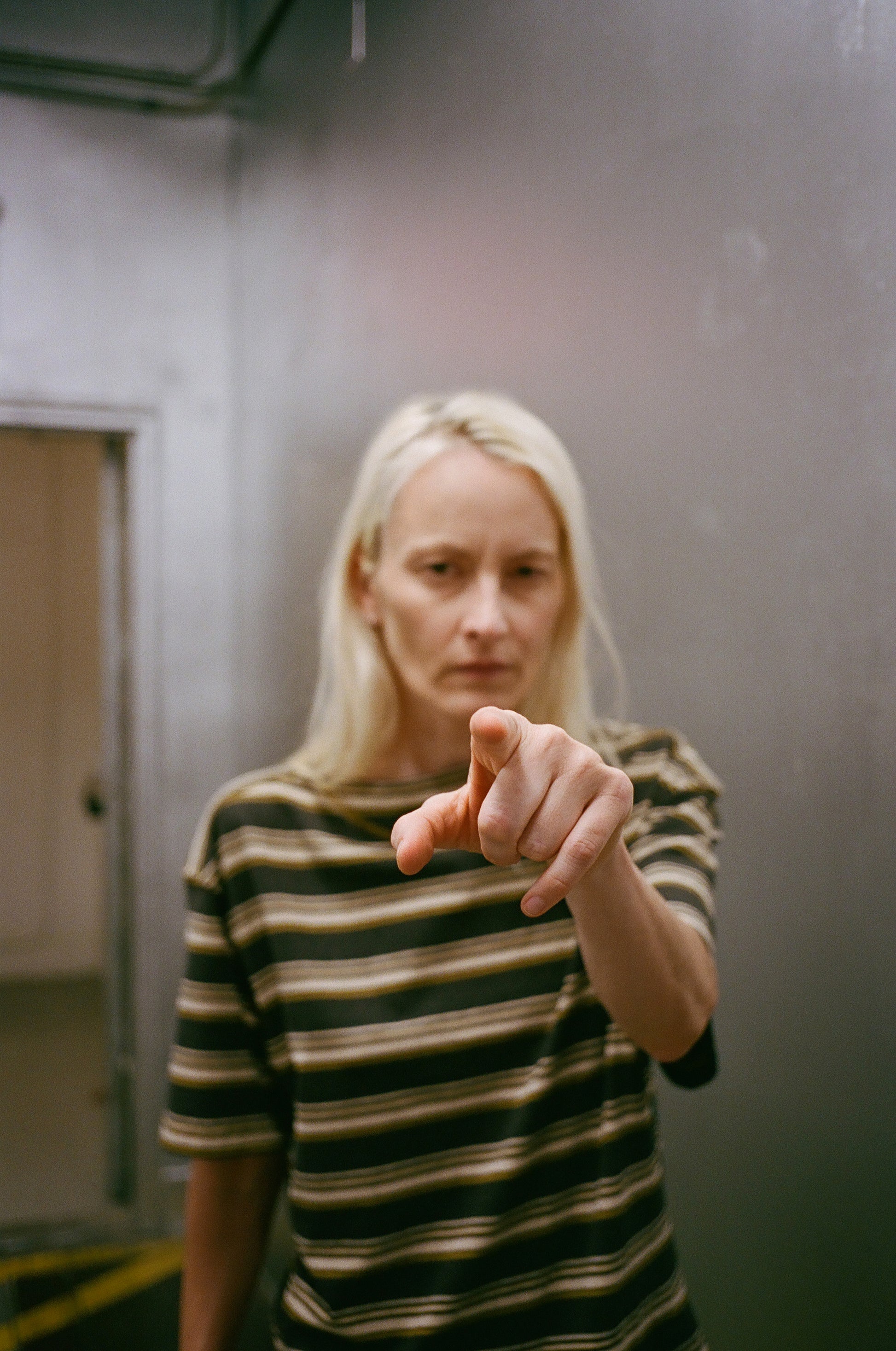 Person wearing a striped shirt pointing towards the camera in an indoor setting
