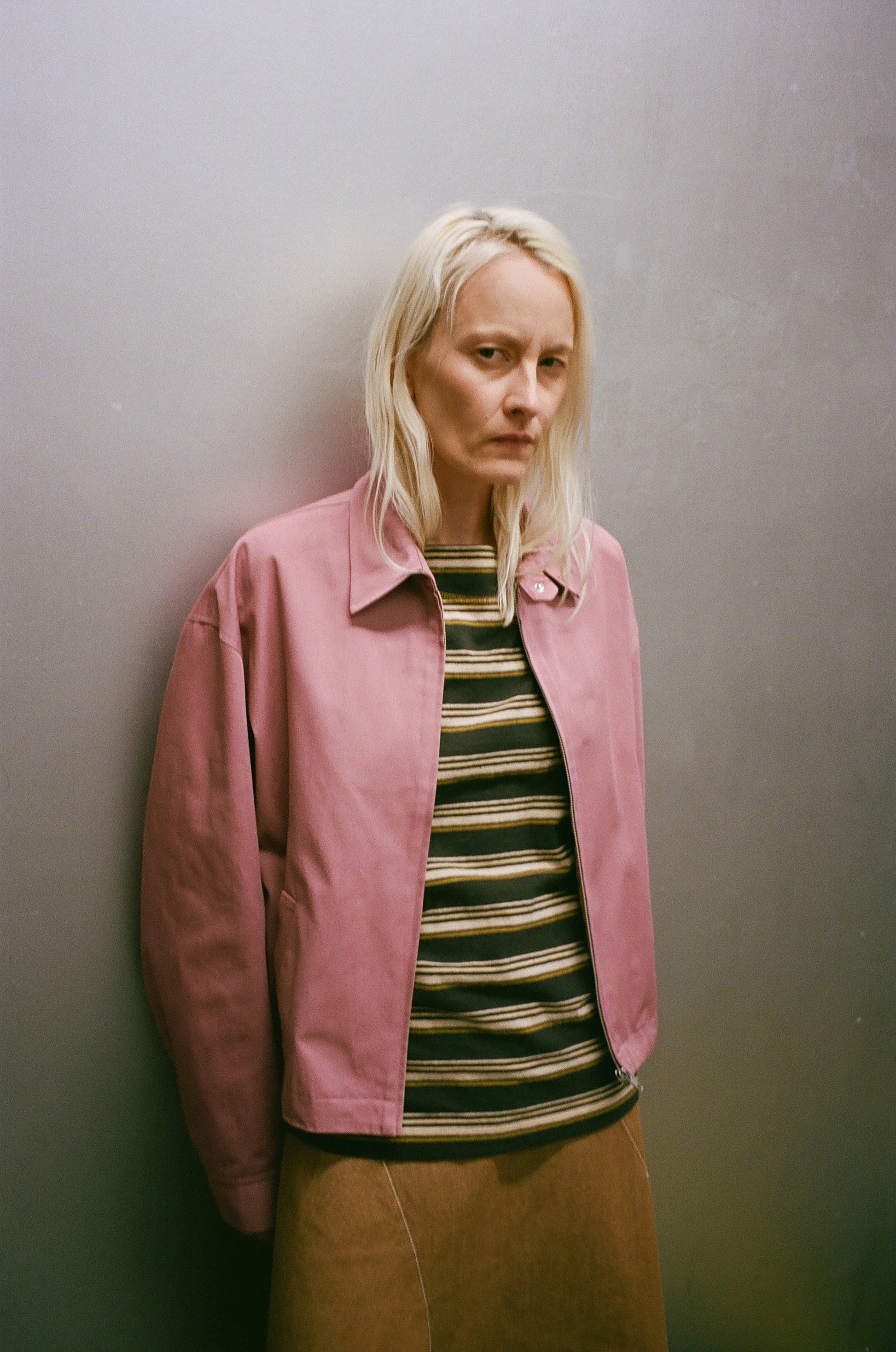 Person wearing a pink jacket over a striped shirt against a plain background