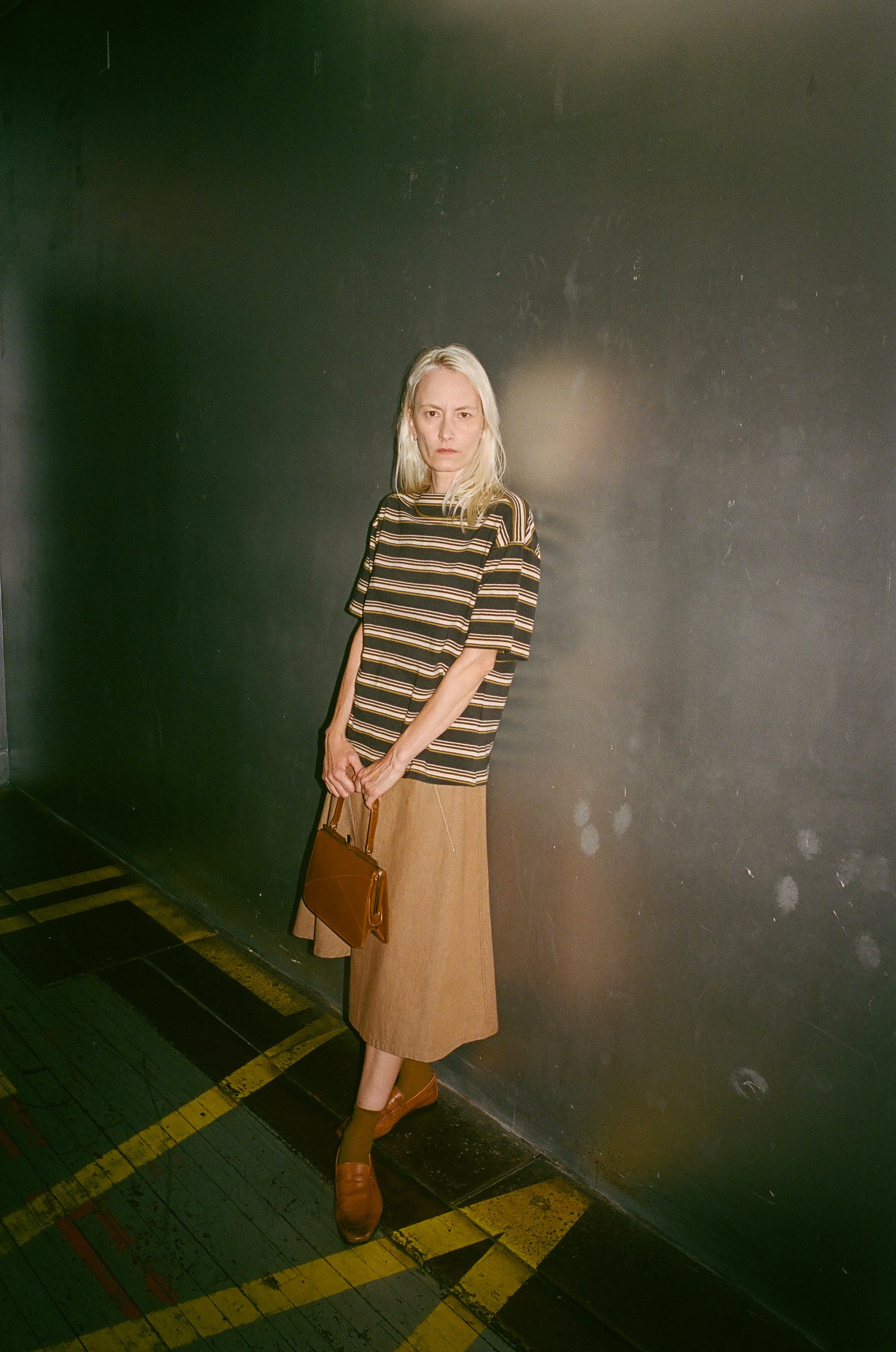 Woman in a striped sweater and skirt standing against a dark wall.