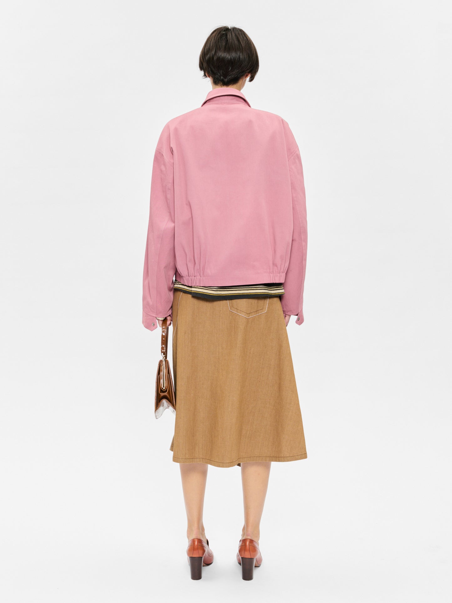 Person wearing a pink jacket and brown skirt on a white background