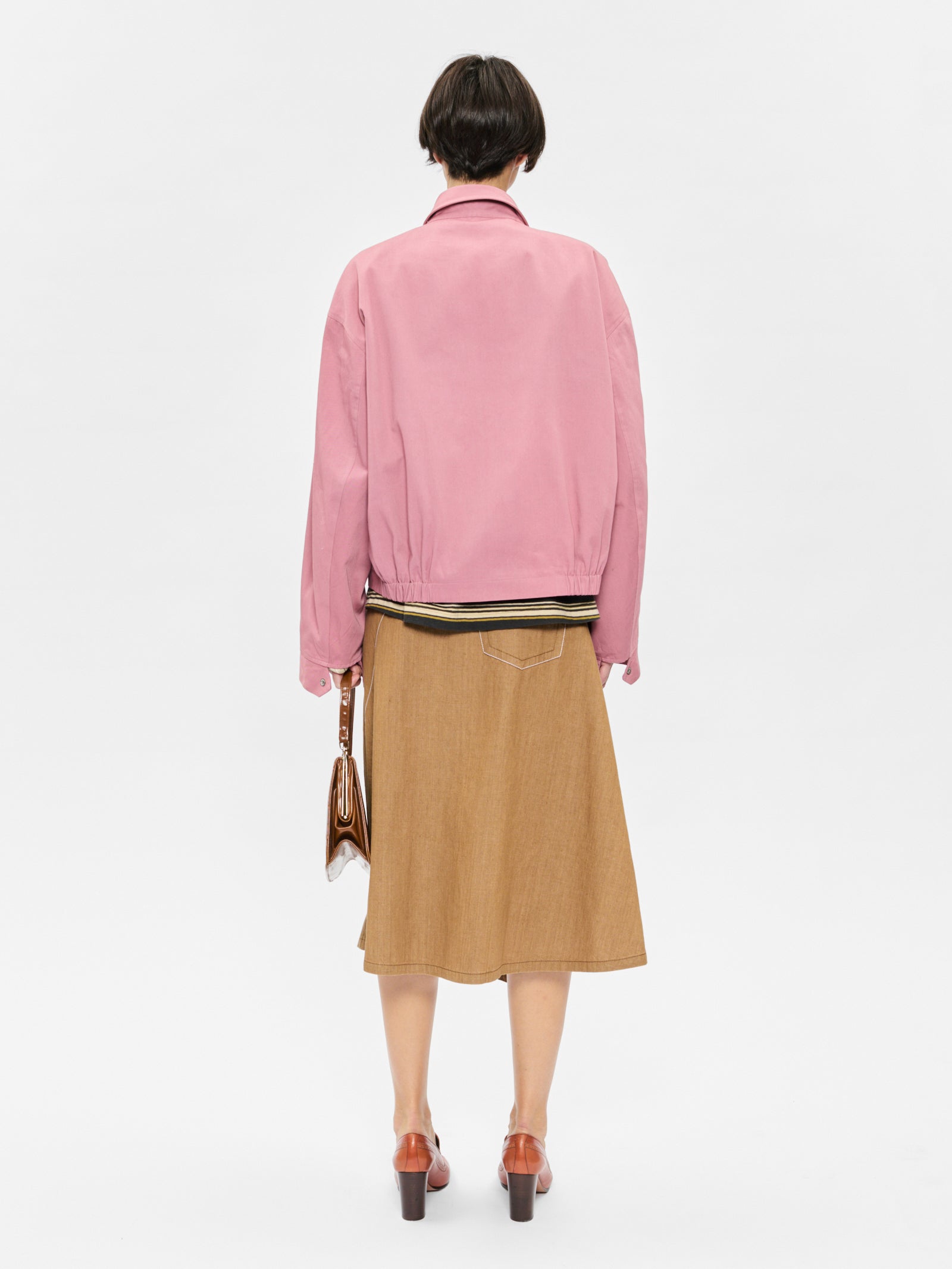 Person wearing a pink jacket and brown skirt on a white background