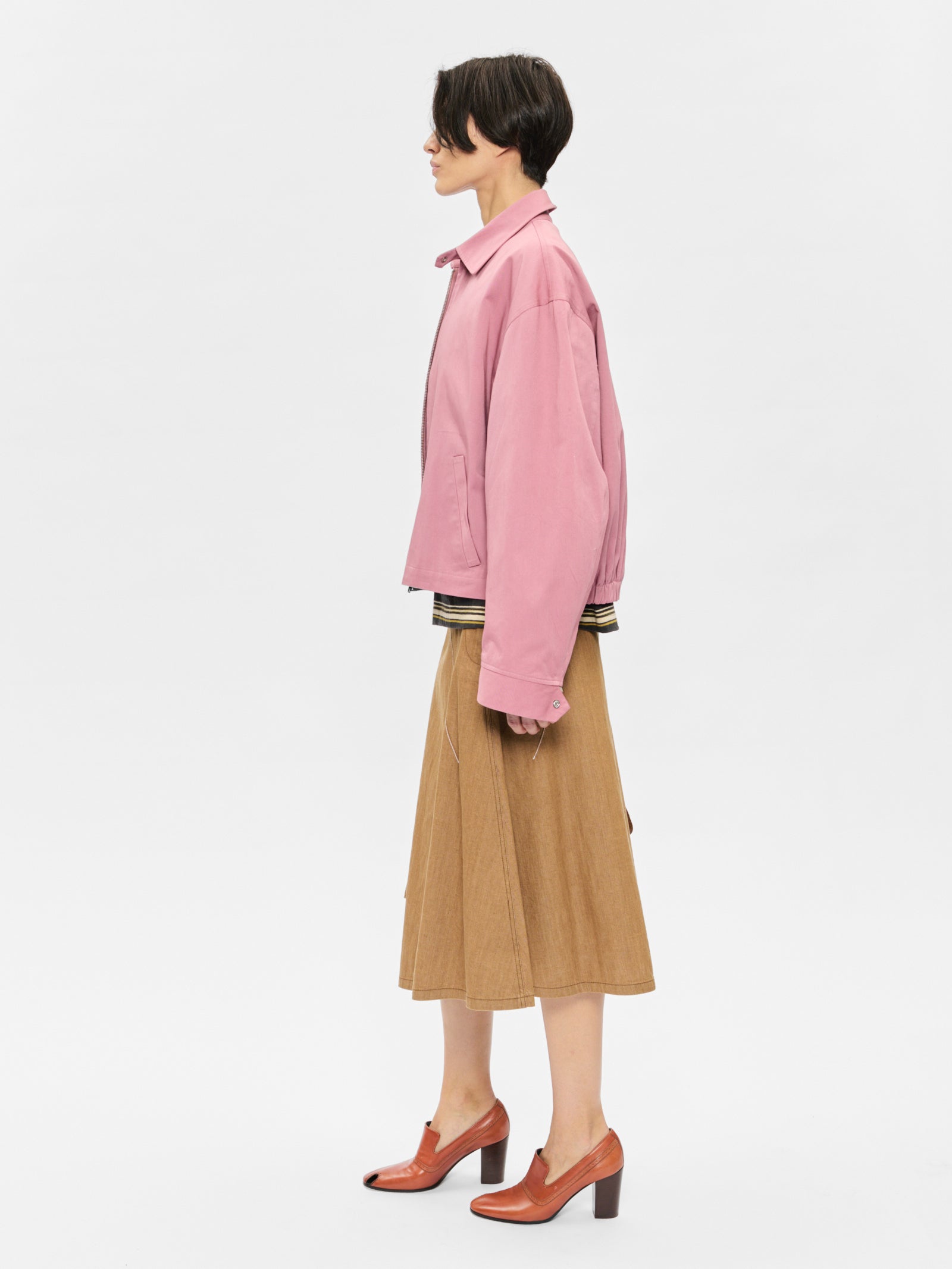 Person wearing a pink jacket and beige skirt on a white background
