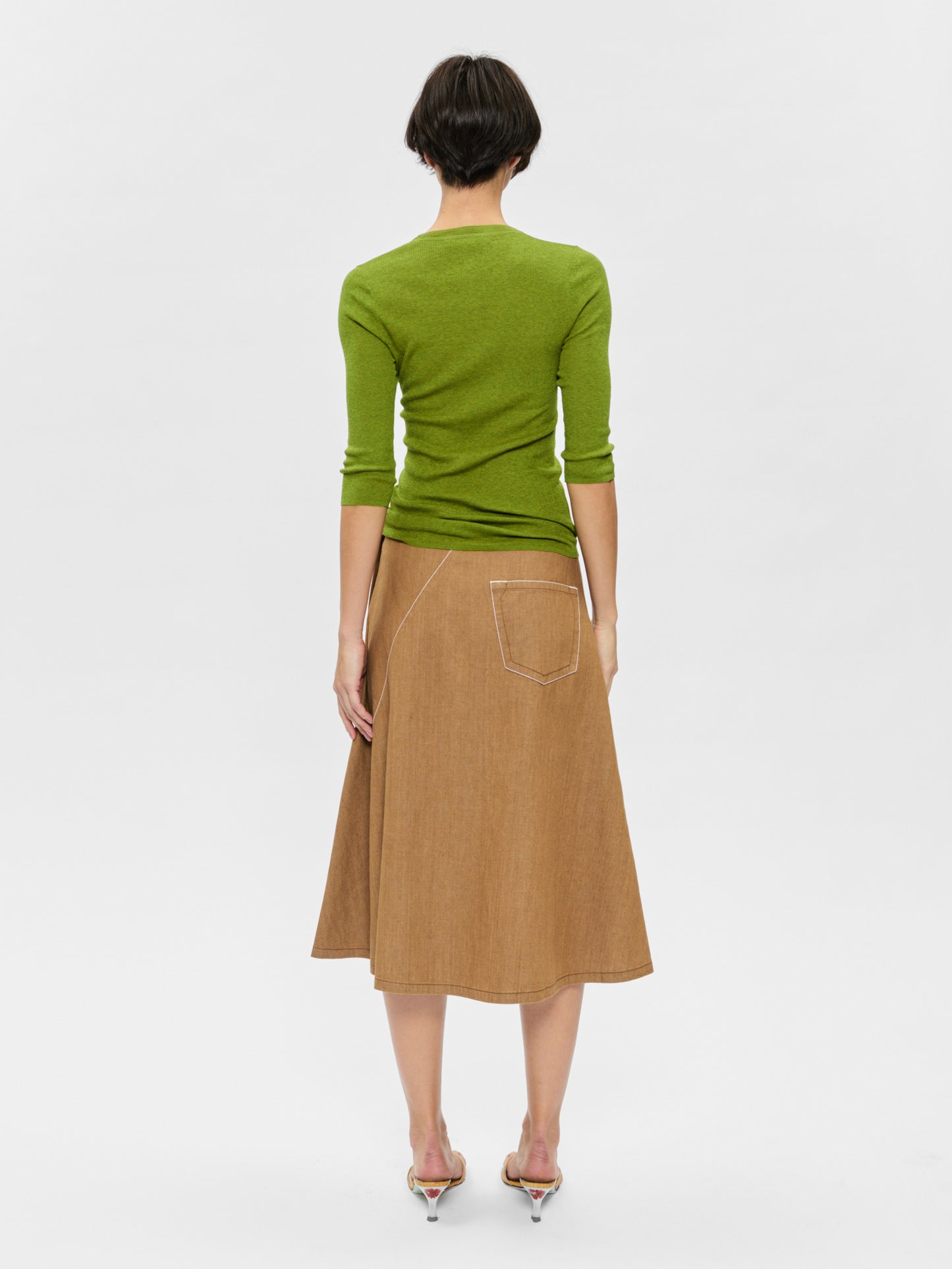 Woman wearing a green top and brown skirt on a white background