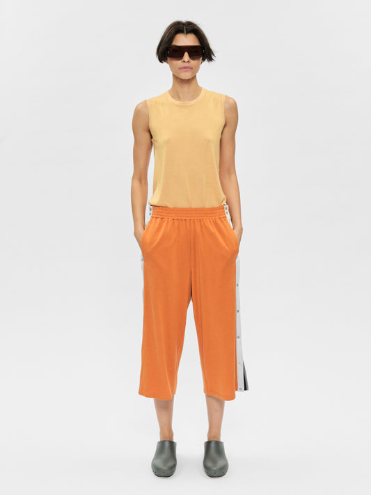 Person wearing a yellow sleeveless top and orange pants with a white background