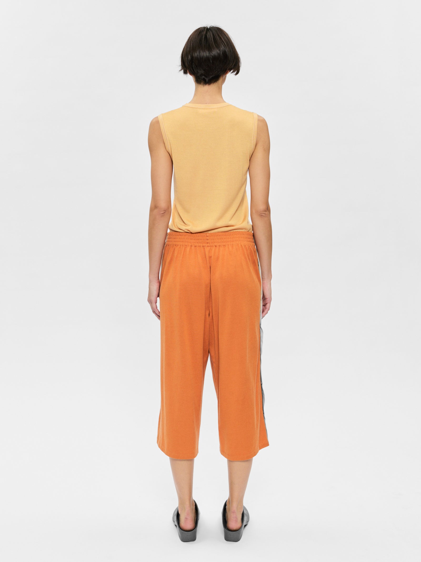 Person wearing a yellow sleeveless top and orange pants on a white background