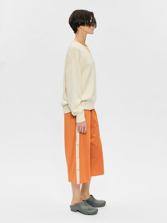 Person wearing a cream sweater and orange pants on a white background