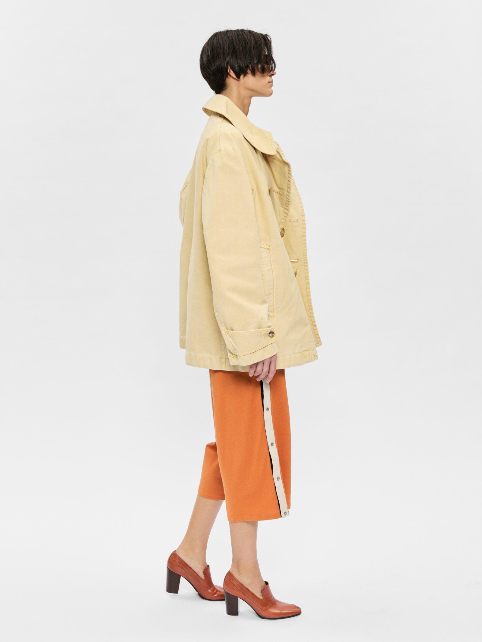 Person wearing a beige coat and orange pants on a white background