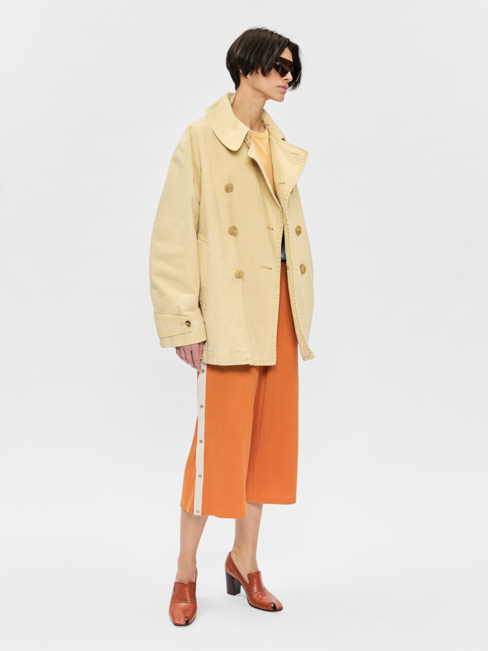 Person wearing a beige coat and orange skirt on a white background