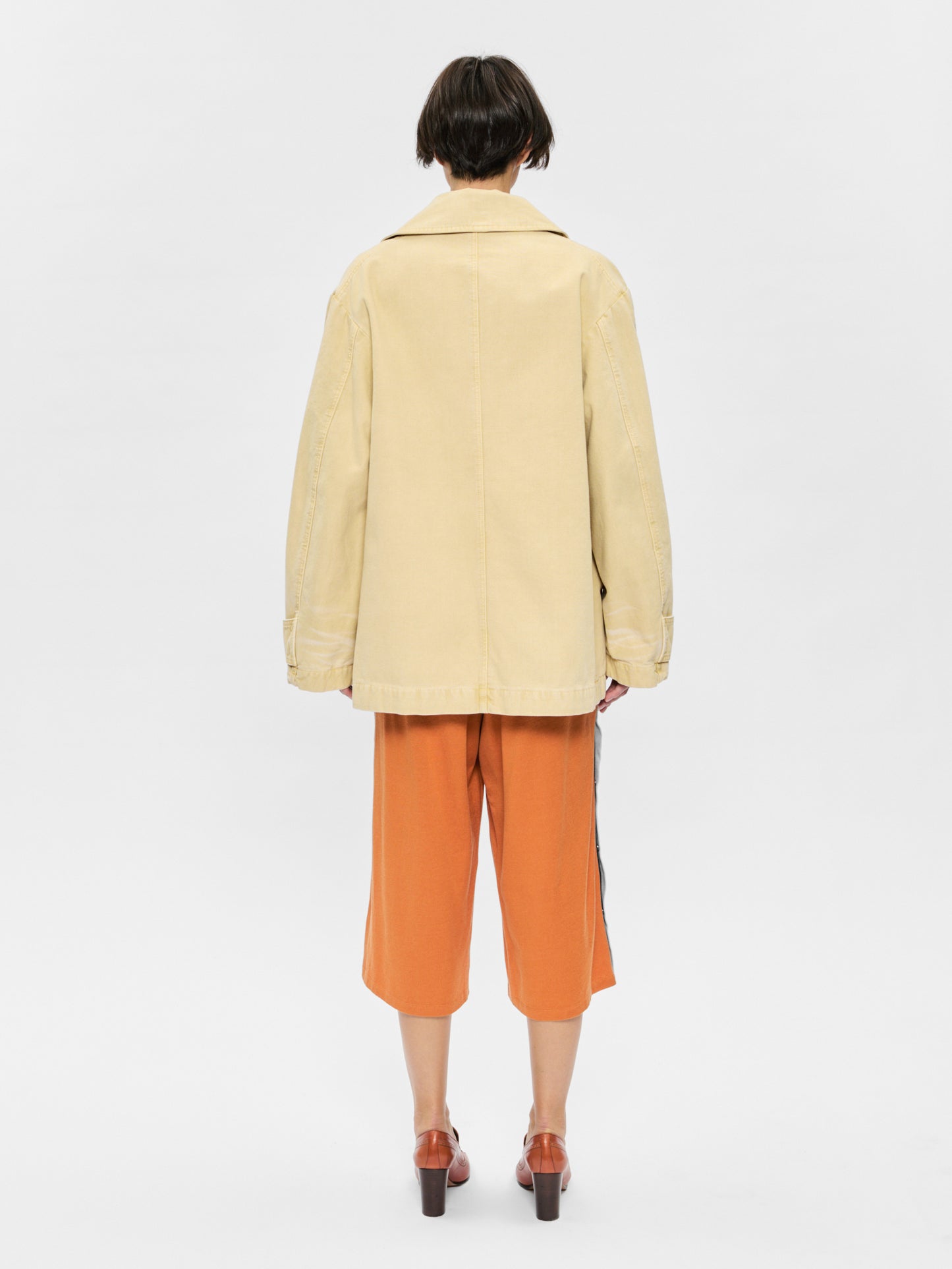 Person wearing a beige coat and orange pants on a white background