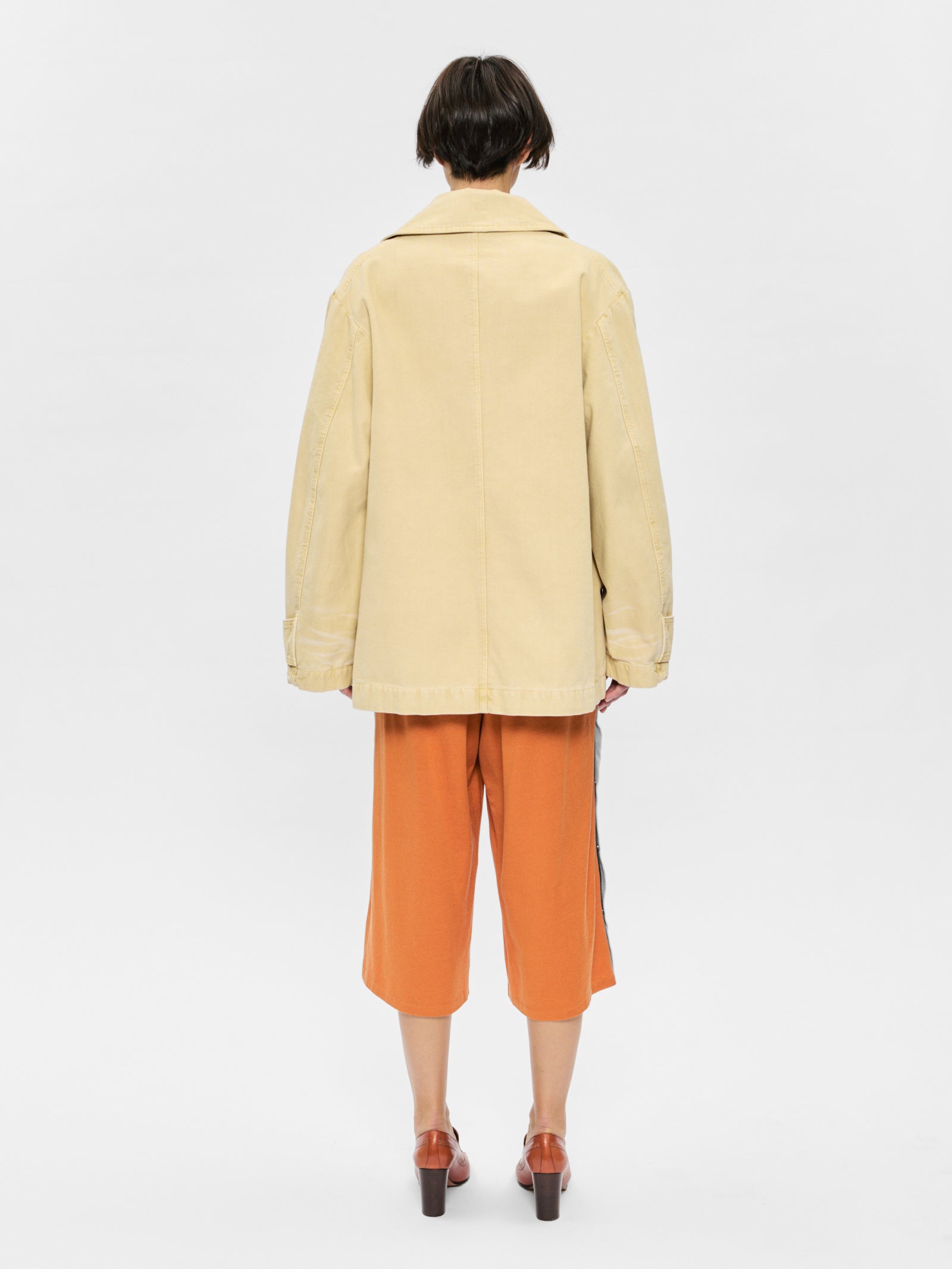 Person wearing a beige coat and orange pants on a white background