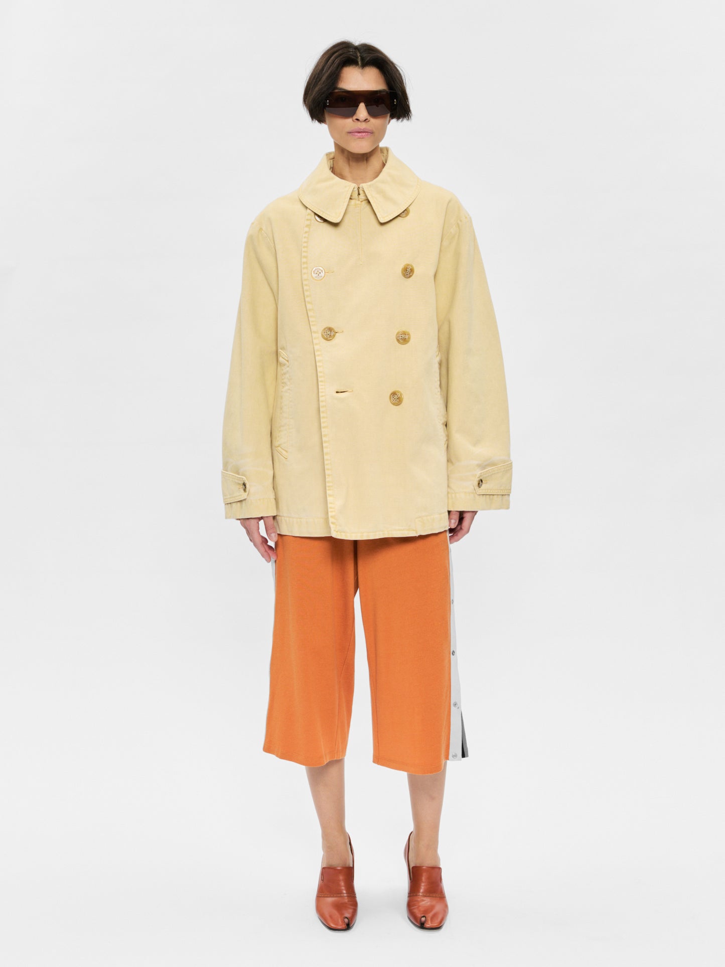 Person wearing a beige coat and orange pants on a white background