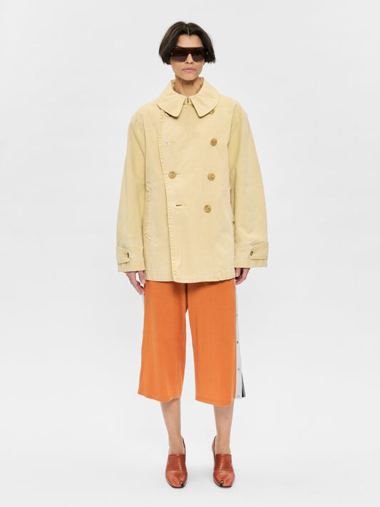 Person wearing a beige coat and orange pants on a white background