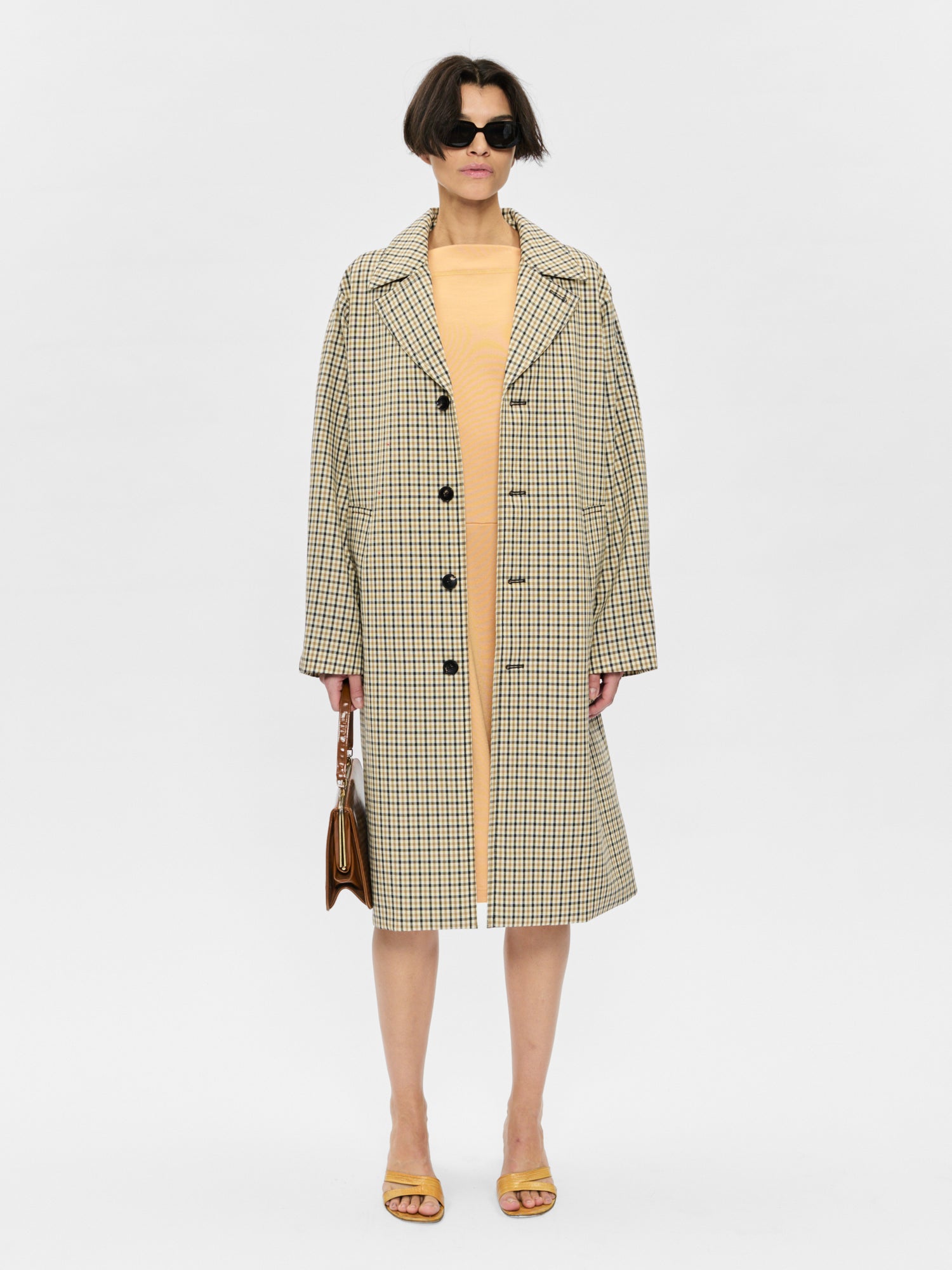 Woman wearing a checkered coat over a yellow dress on a white background