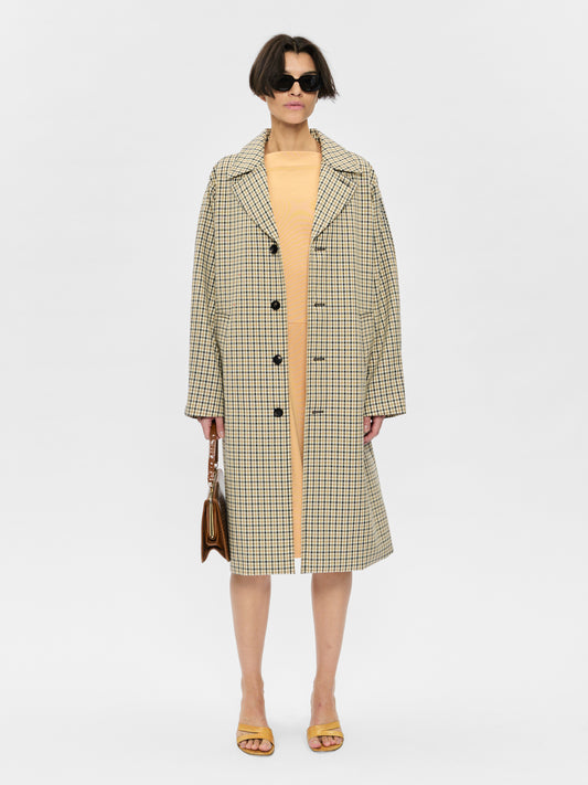 Woman wearing a checkered coat over a yellow dress on a white background