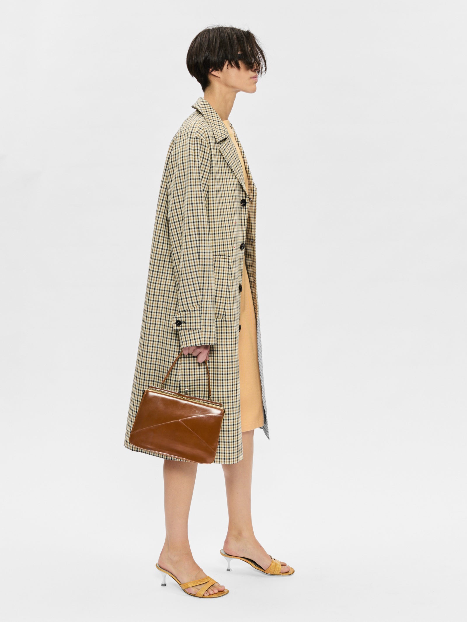 Person wearing a plaid coat with a brown handbag on a white background