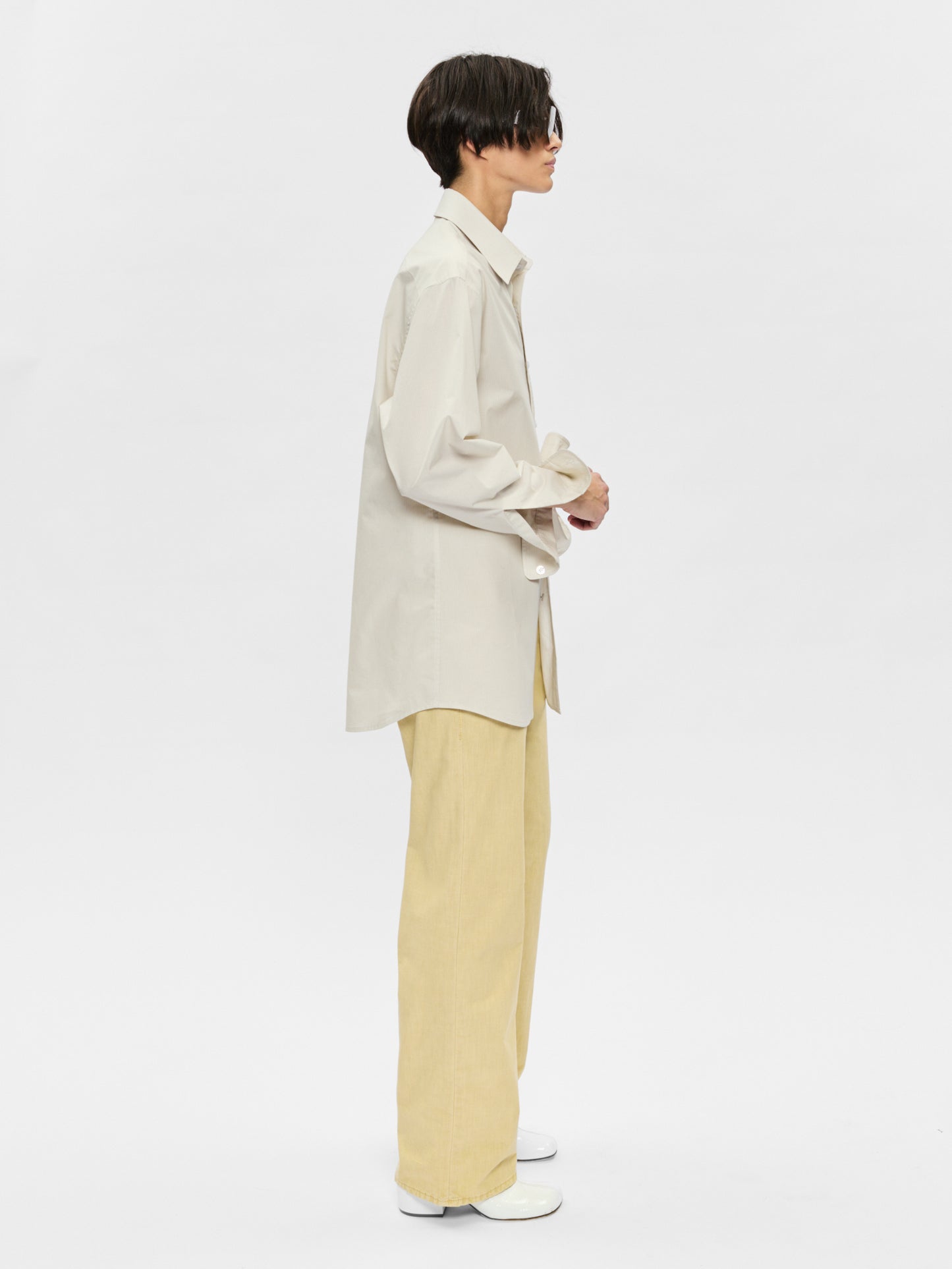 Person wearing a beige shirt and light yellow pants on a white background