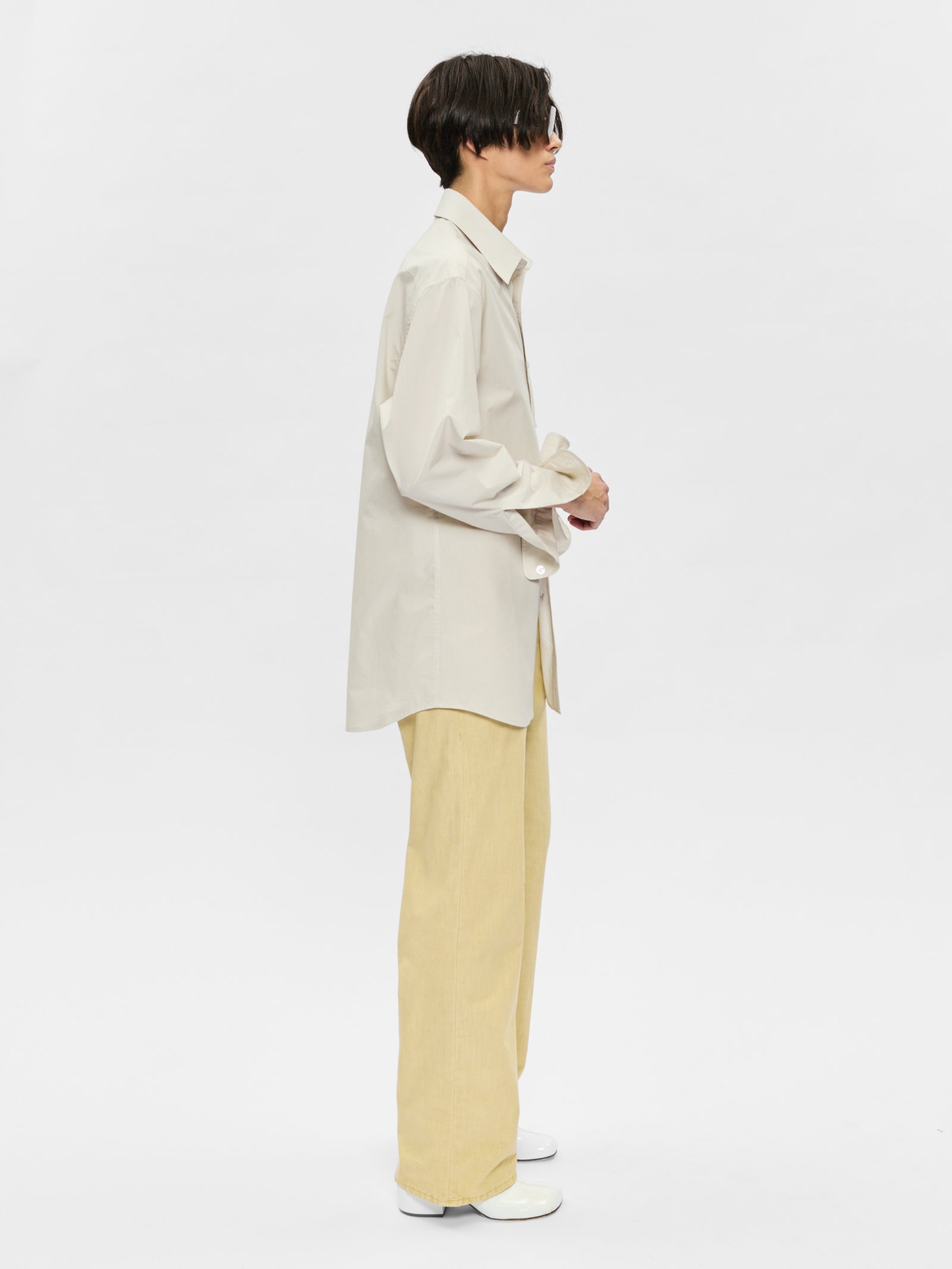 Person wearing a beige shirt and light yellow pants on a white background