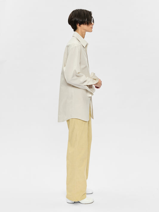 Person wearing a beige shirt and light yellow pants on a white background
