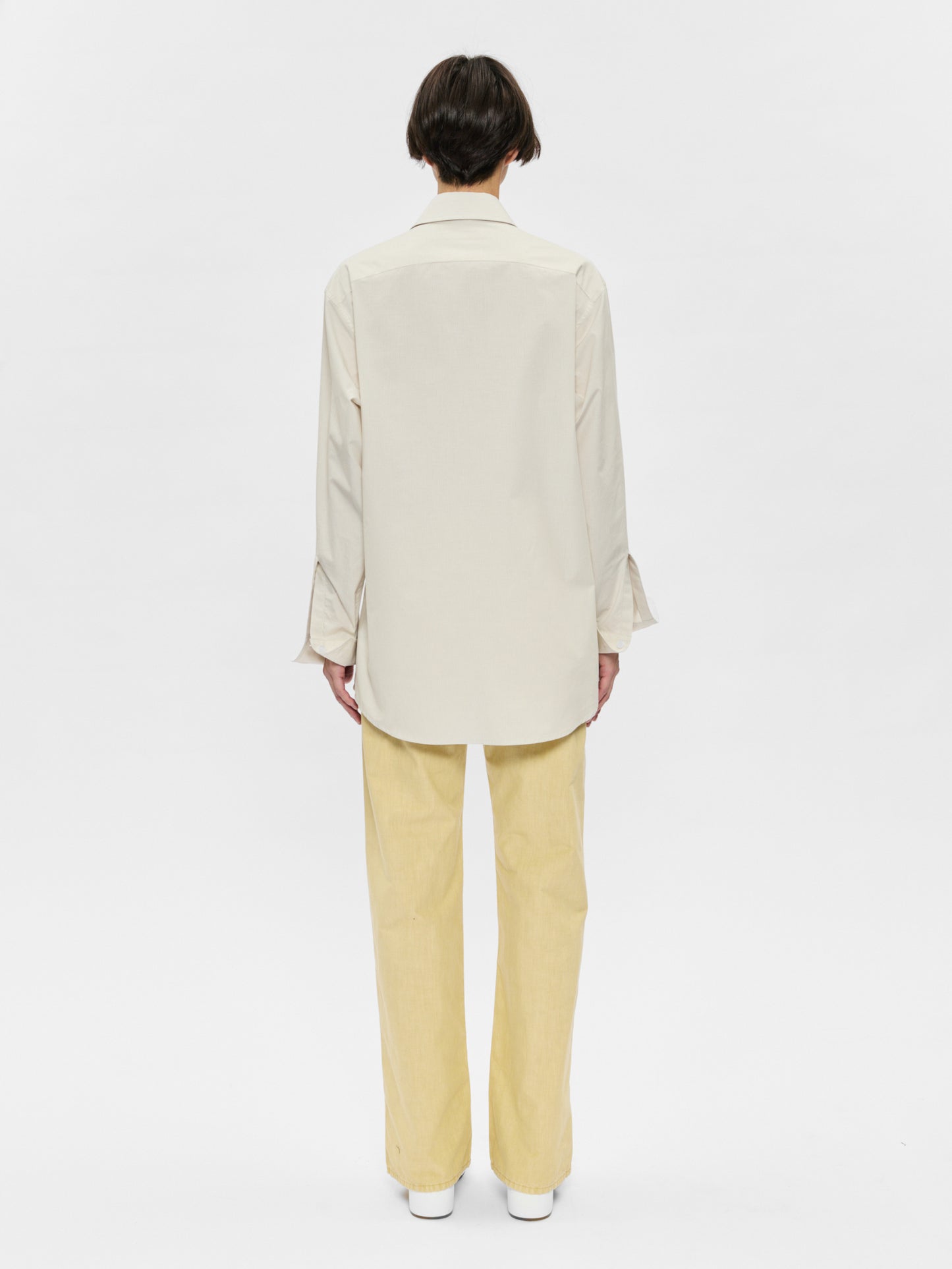 Person wearing a beige blazer and yellow pants on a white background