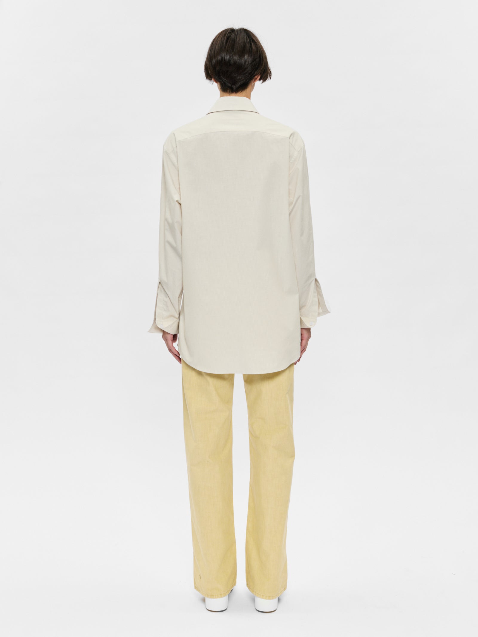 Person wearing a beige blazer and yellow pants on a white background