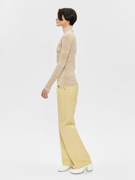Person wearing a beige turtleneck sweater and yellow pants on a white background