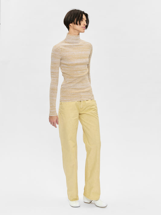 Woman wearing a beige turtleneck sweater and yellow pants on a white background