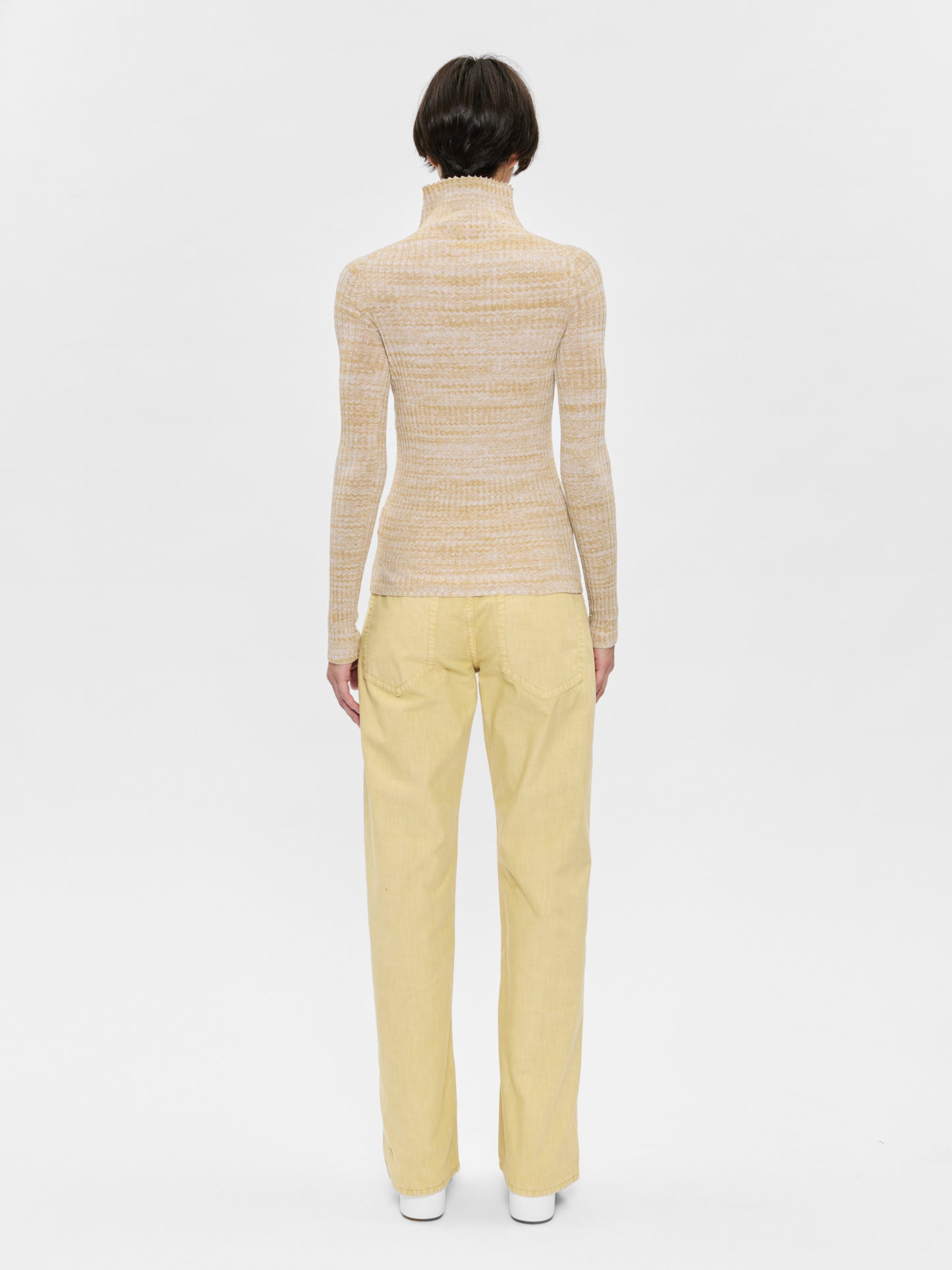 Person wearing a beige sweater and yellow pants on a white background