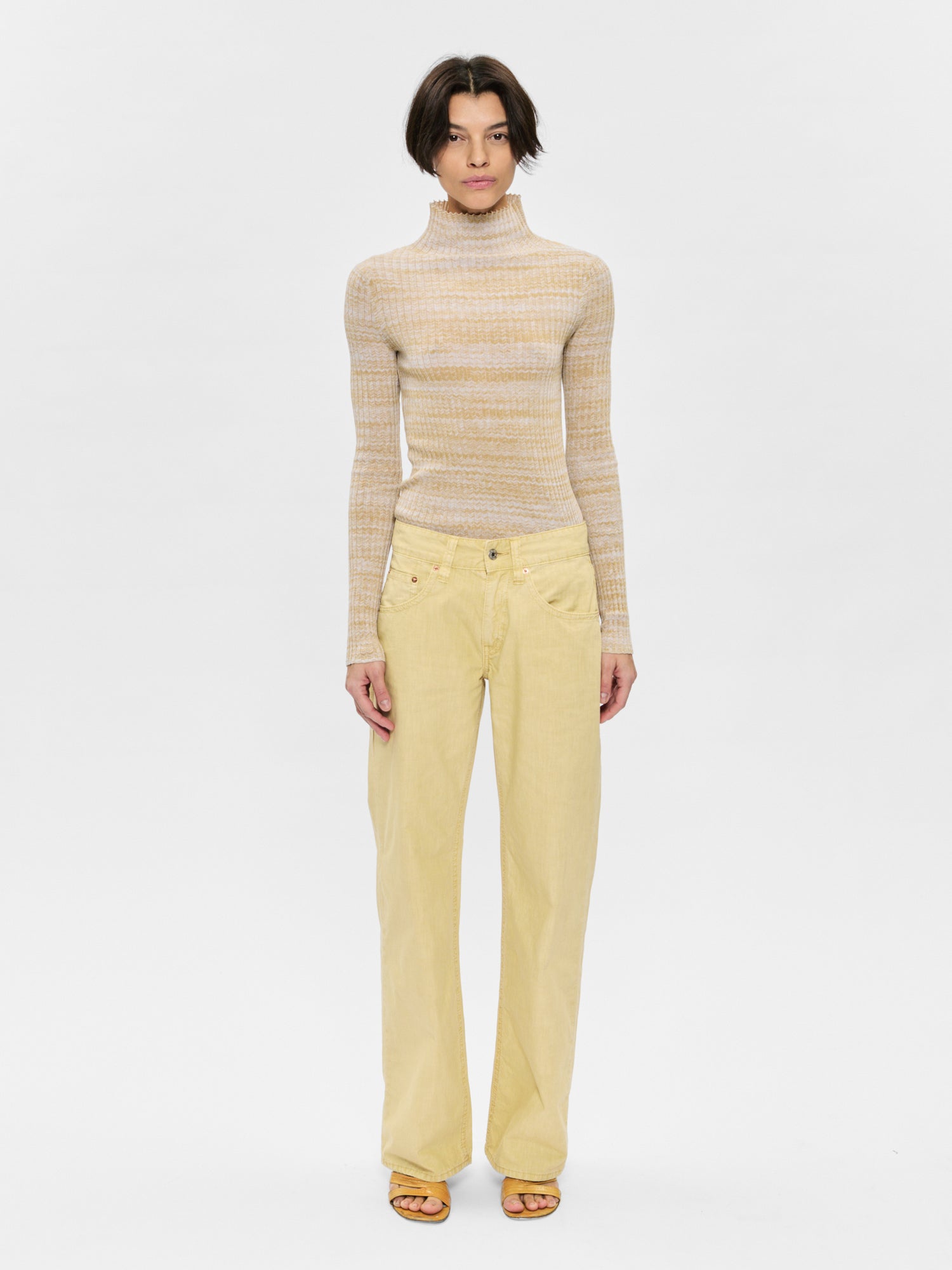 Woman wearing a beige turtleneck sweater and yellow pants on a white background