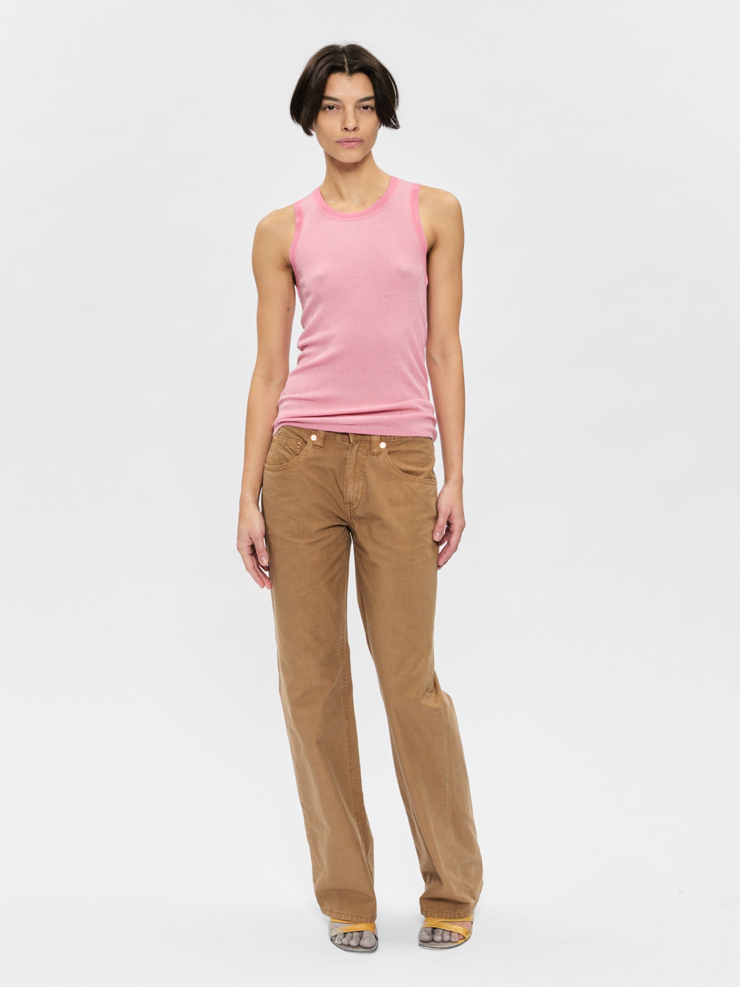 Woman wearing a pink tank top and brown pants on a white background