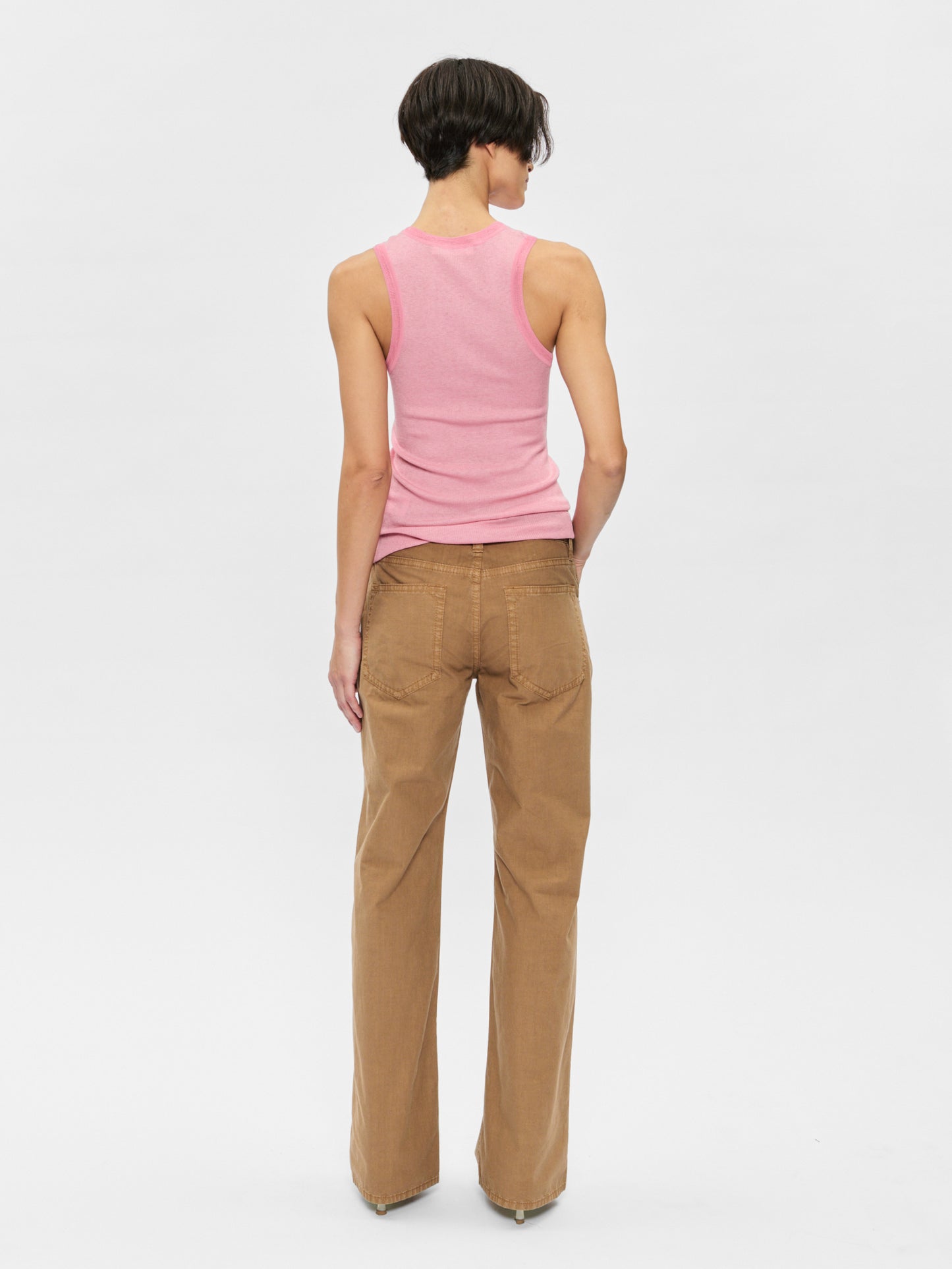 Person wearing a pink sleeveless top and brown pants on a white background