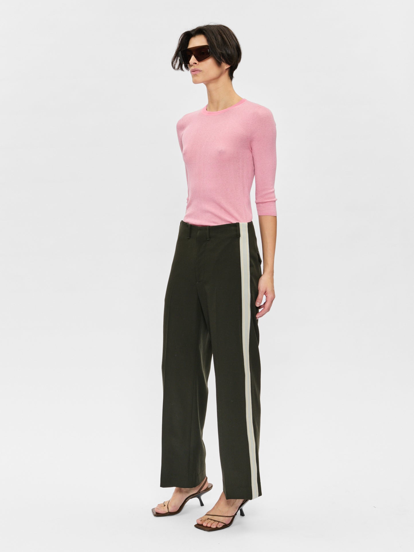 Woman wearing a pink sweater and black pants with white stripes on a white background
