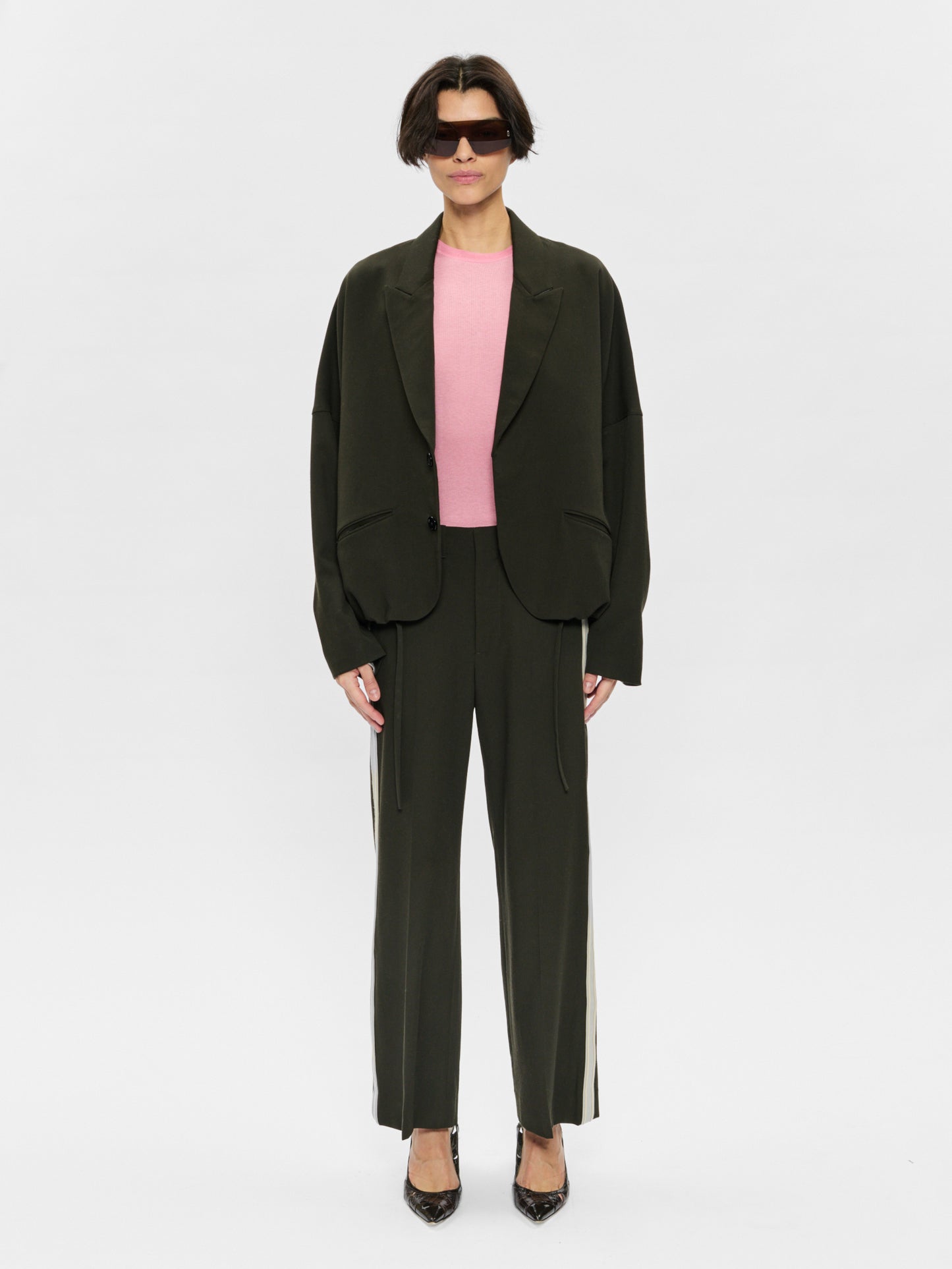 Person wearing a dark green suit with a pink top on a white background