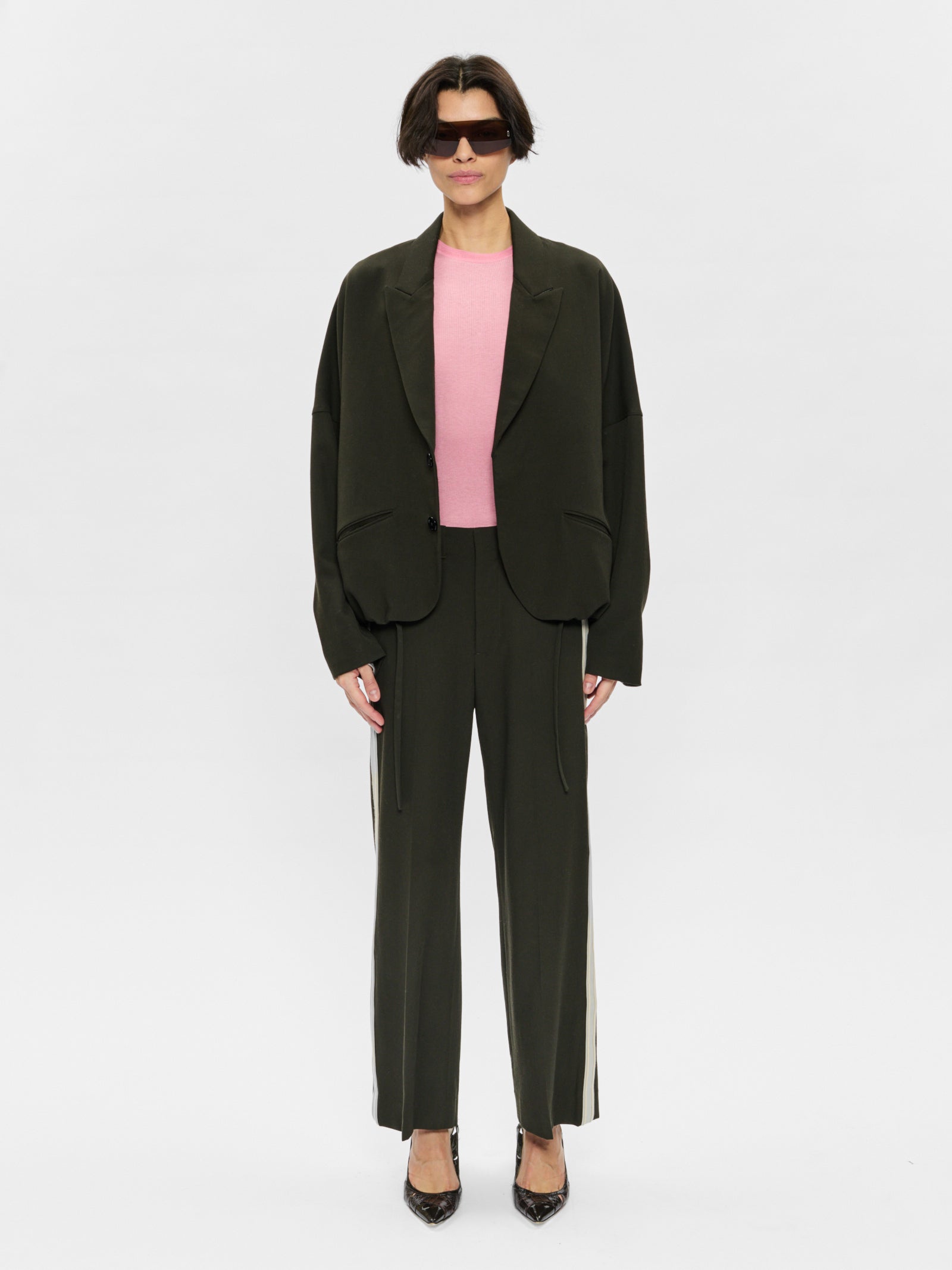 Person wearing a dark green suit with a pink top on a white background