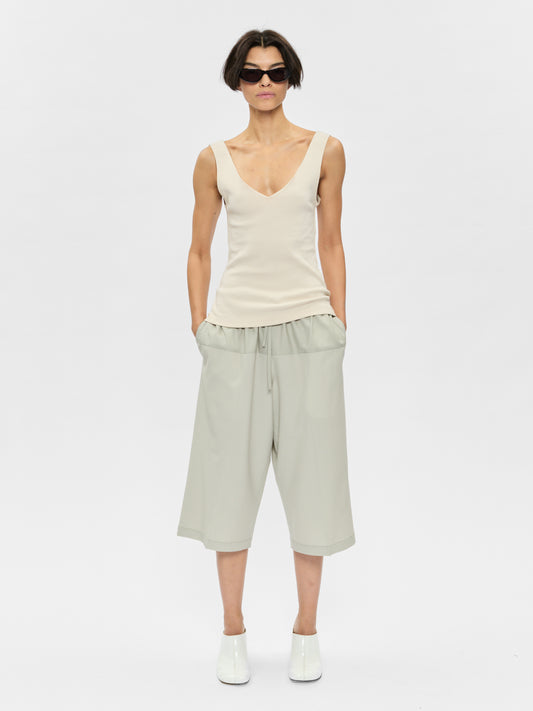 Woman wearing a white sleeveless top and light green pants on a white background