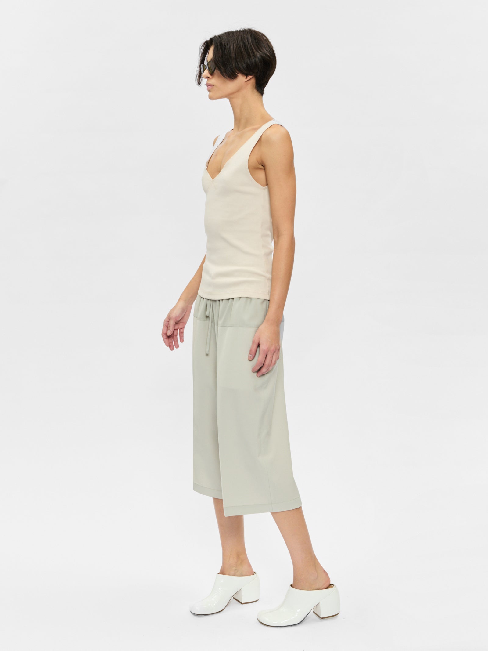 Woman wearing a white sleeveless top and light green pants on a white background