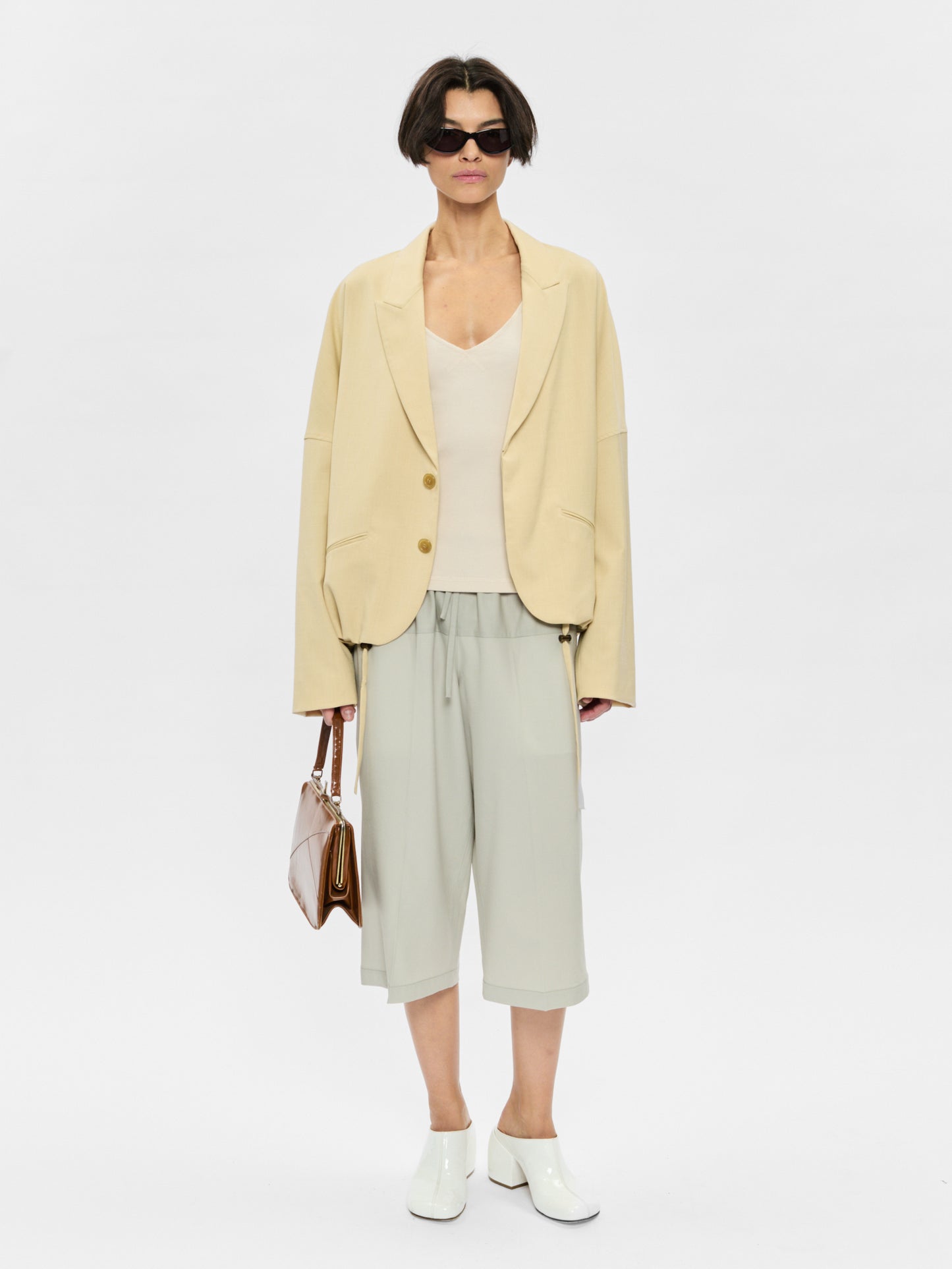 Woman wearing a light yellow blazer, white top, and light green pants on a white background