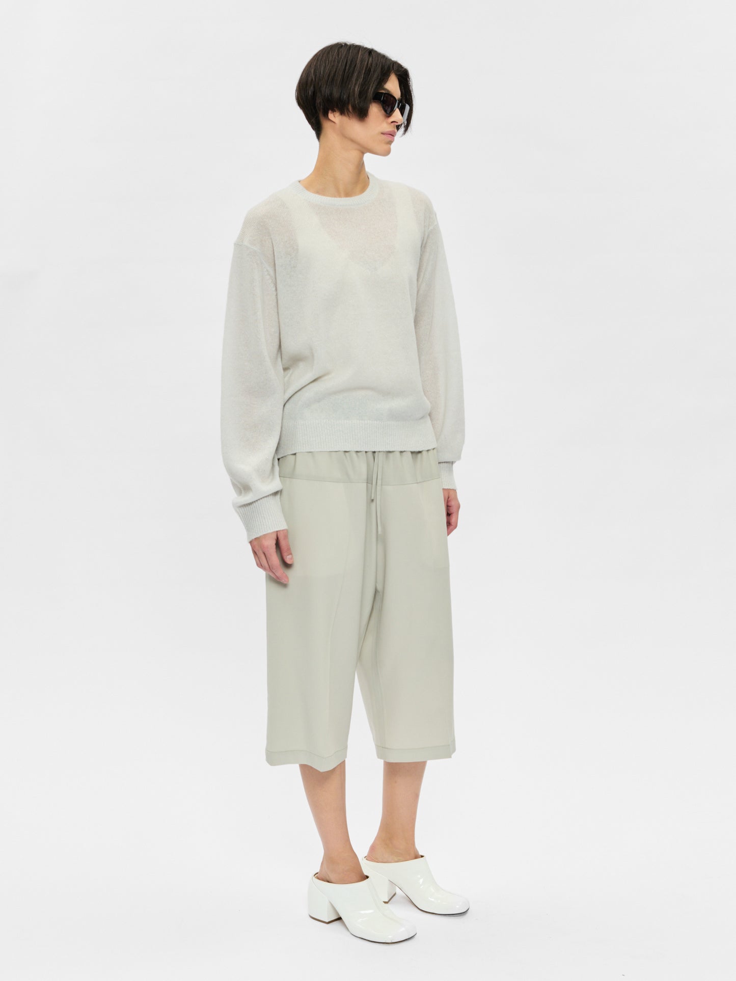 Person wearing a light gray sweater and pants on a white background