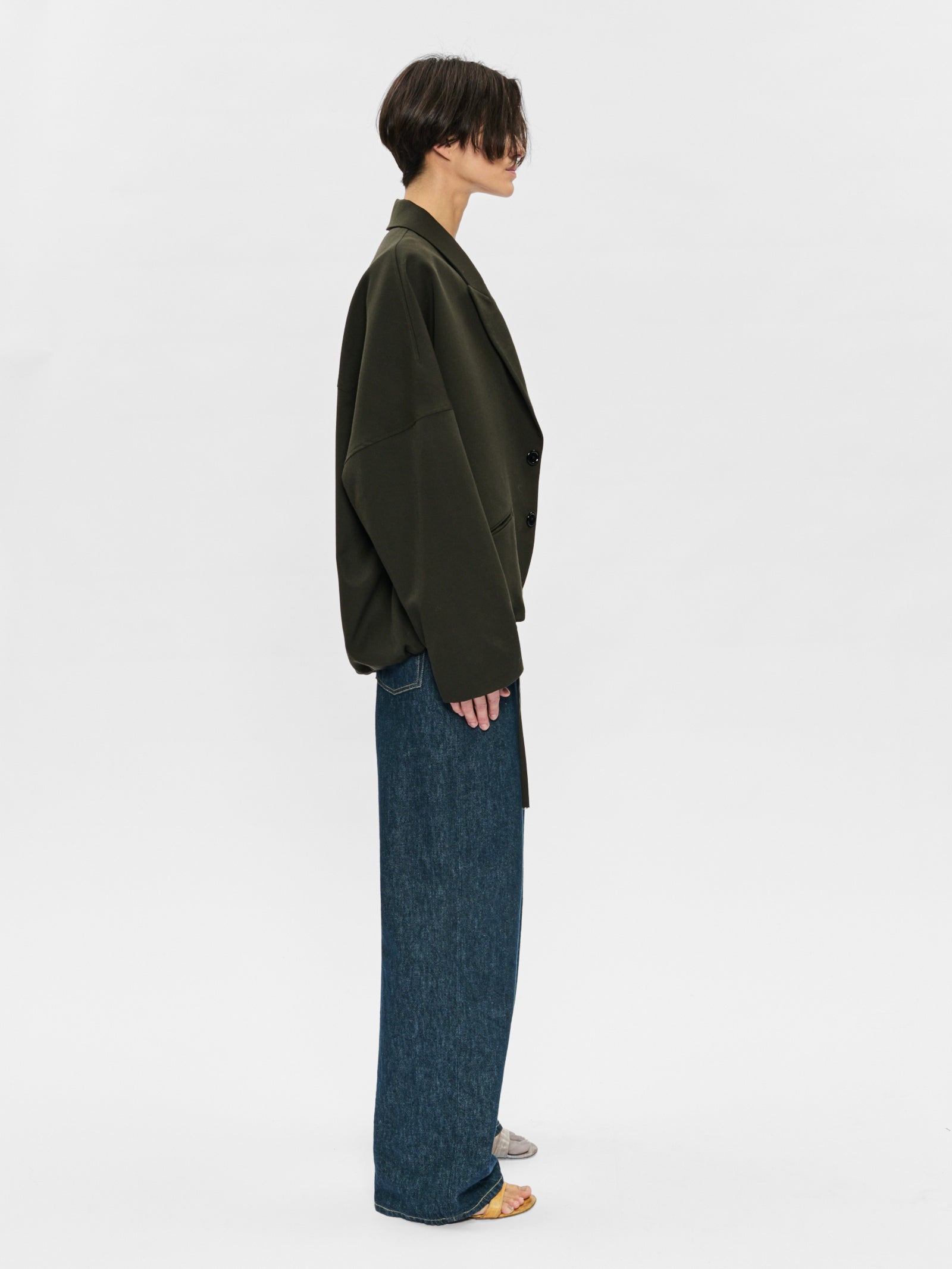 Person wearing a green jacket and blue jeans on a white background