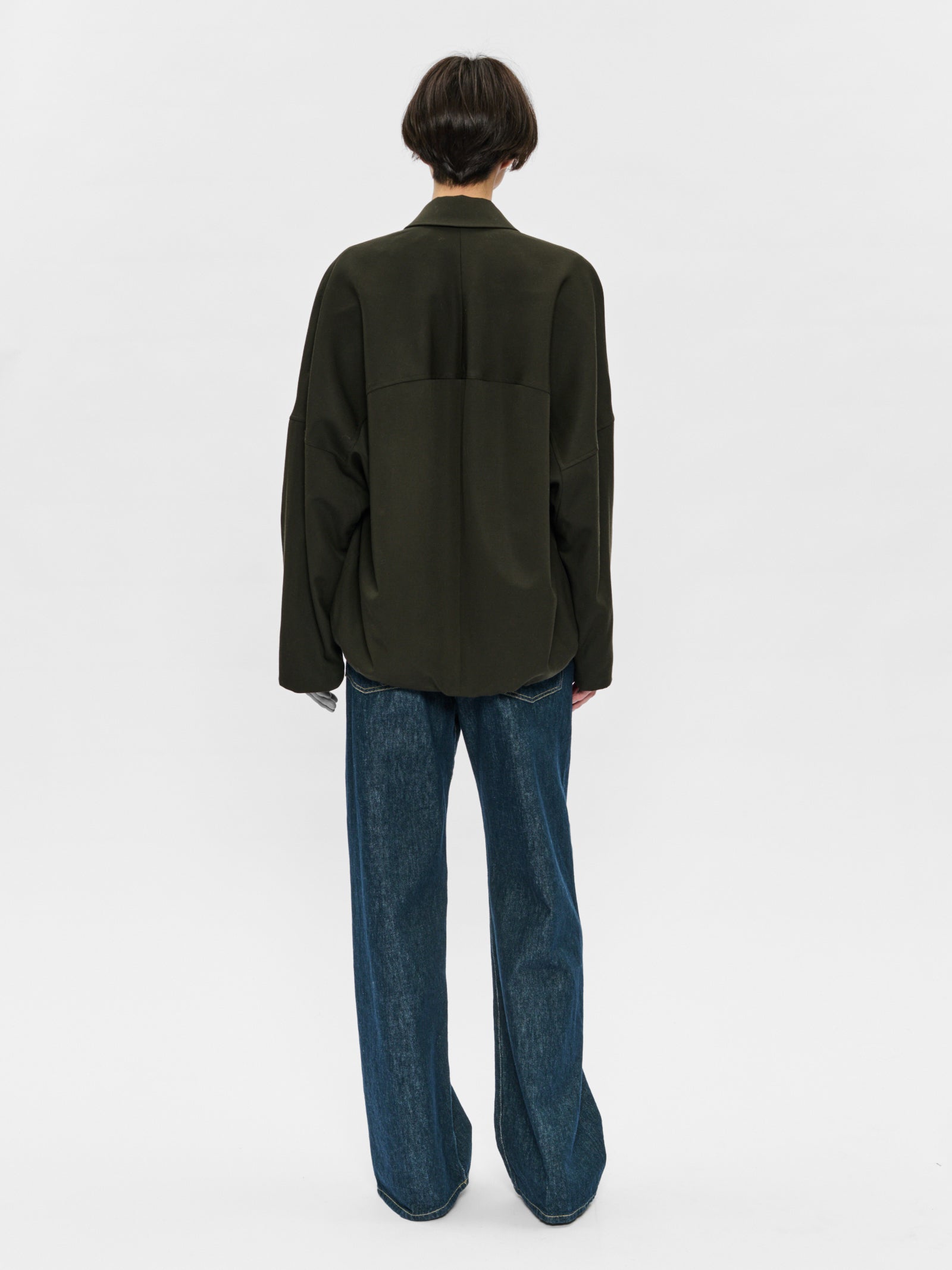 Person wearing a dark green jacket and blue jeans on a white background