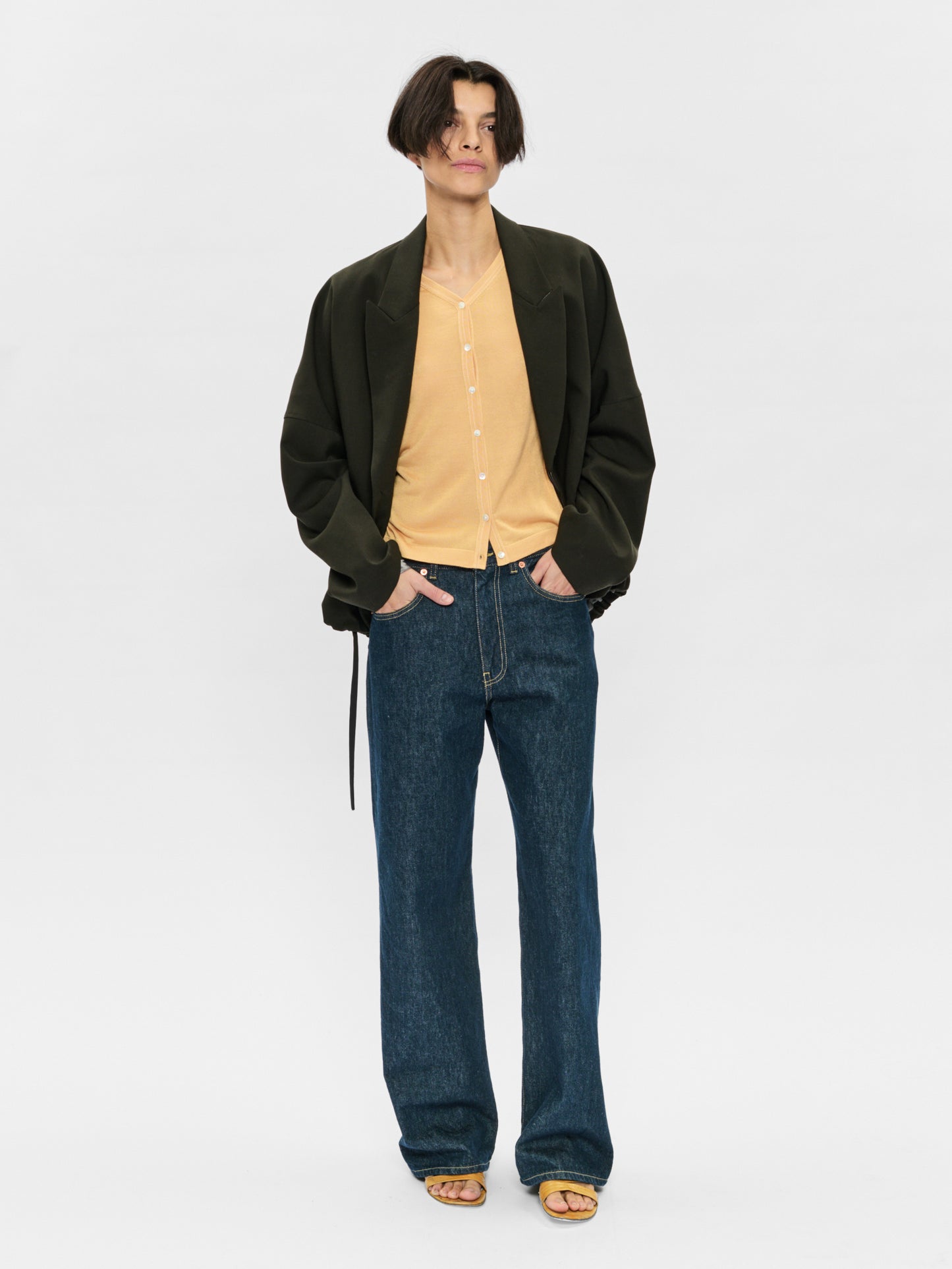 Person wearing a black jacket, beige shirt, and blue jeans on a white background