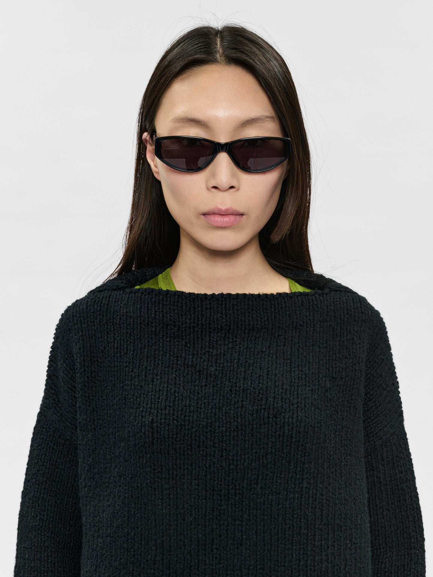Person wearing a black sweater and dark sunglasses on a white background