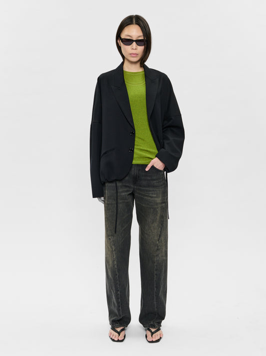 Person wearing a black blazer, green shirt, and gray pants on a white background