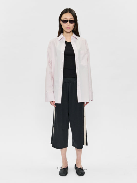 Person wearing a light pink shirt and black pants on a white background