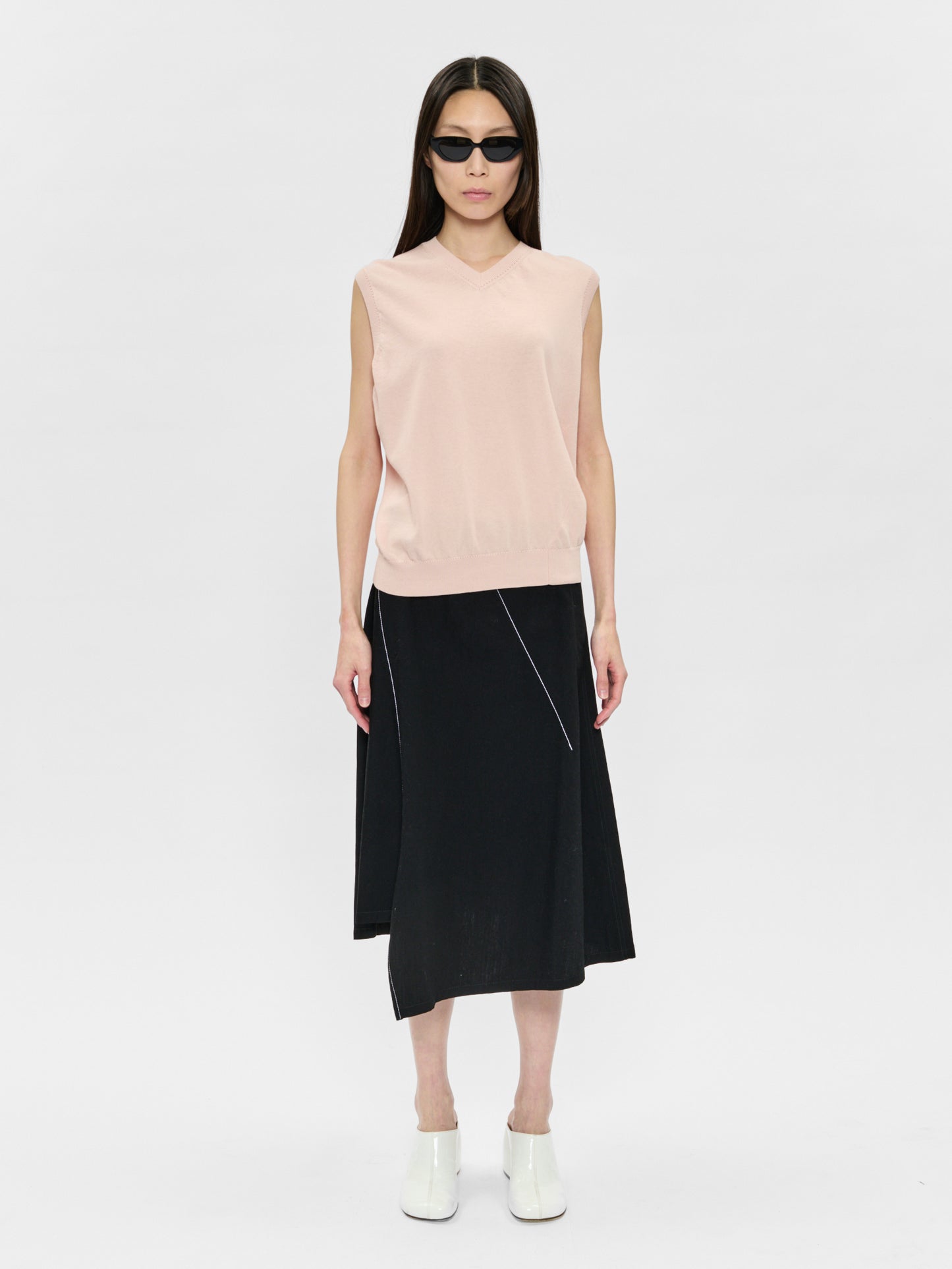 Woman wearing a light pink sleeveless top and black skirt on a white background