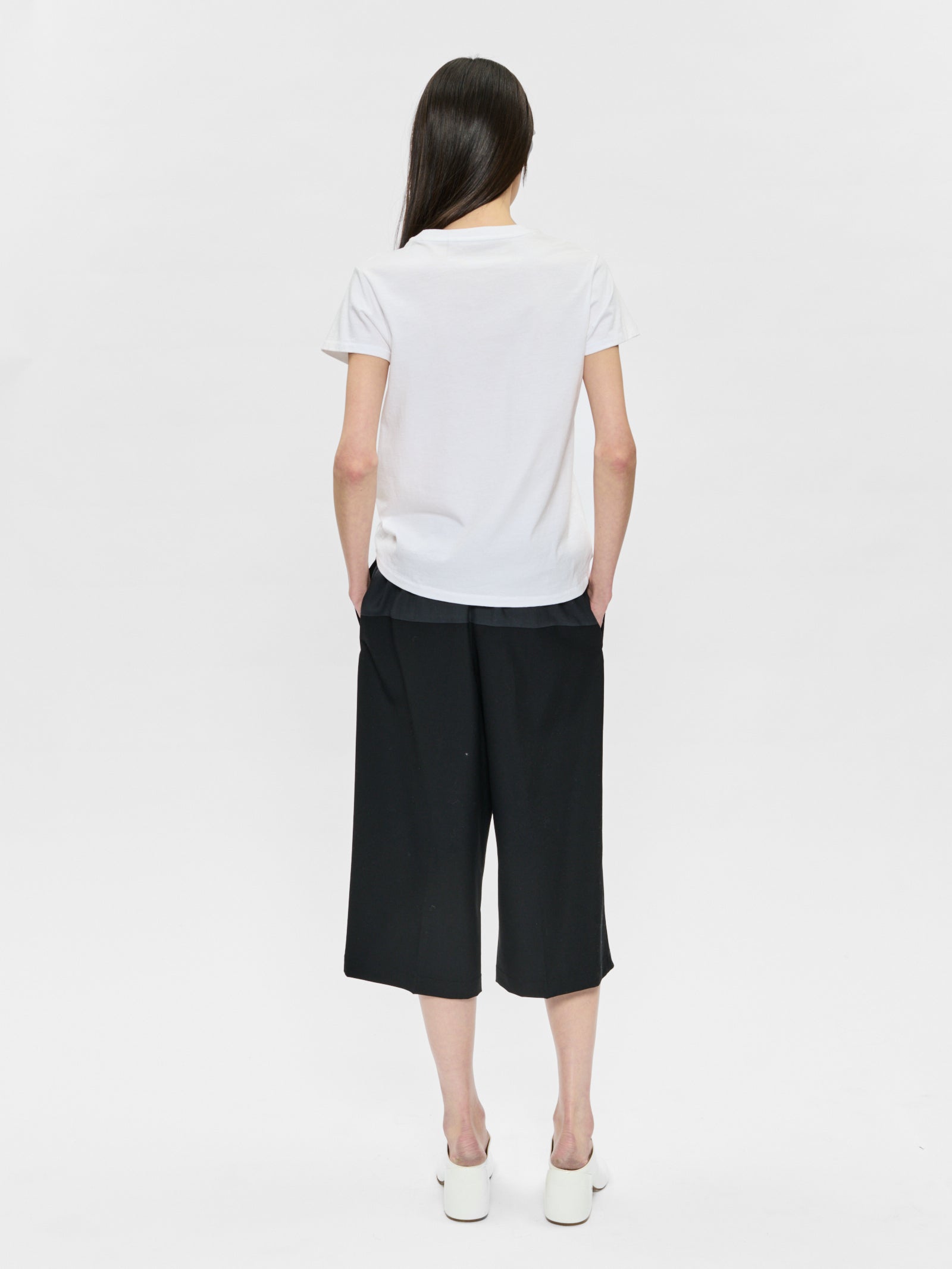 Person wearing a white t-shirt and black pants on a white background