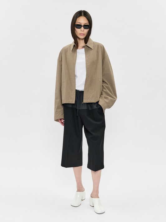 Person wearing a beige jacket, white shirt, black pants, and sunglasses on a white background