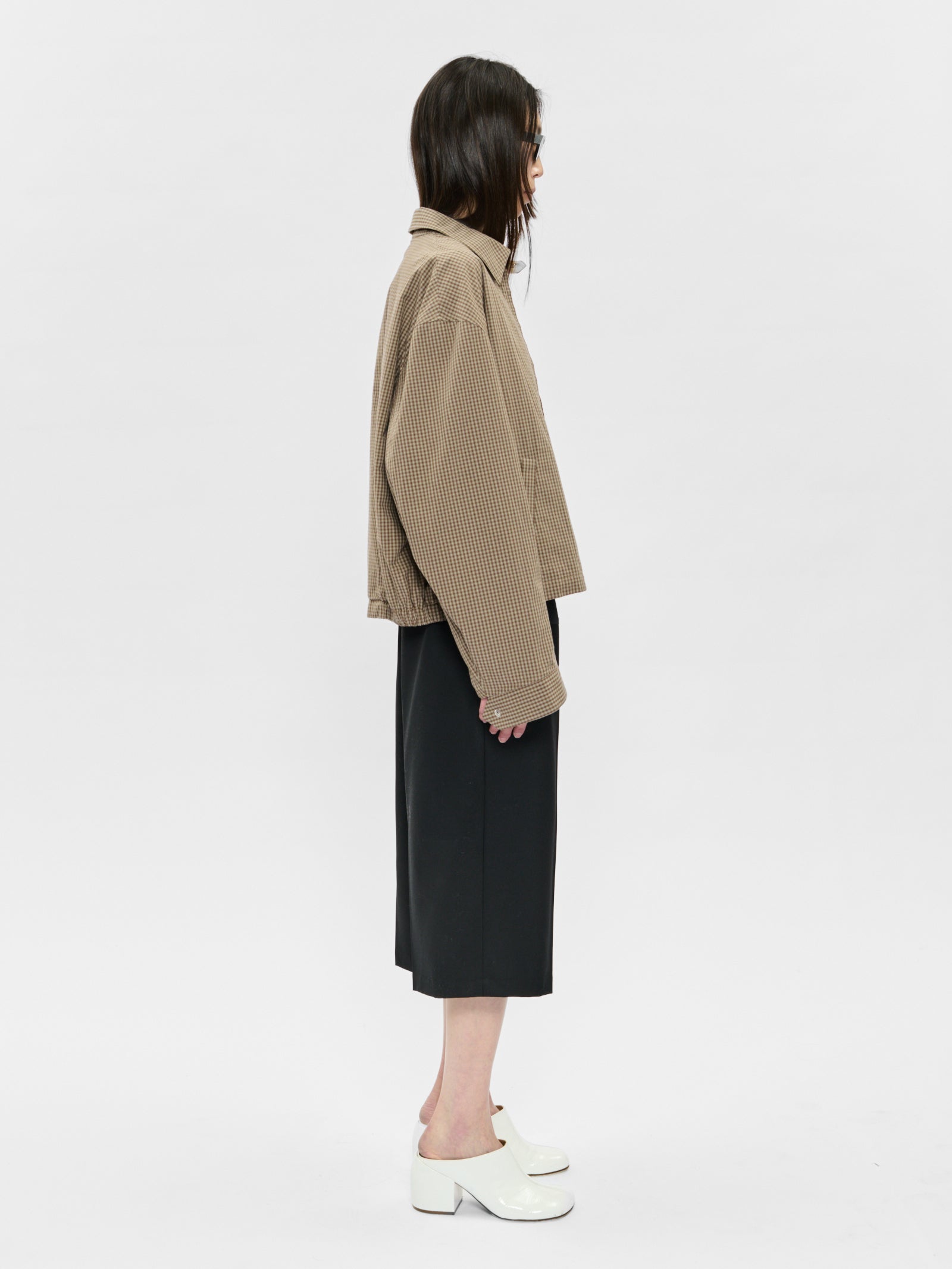 Person wearing a beige jacket and black skirt on a white background